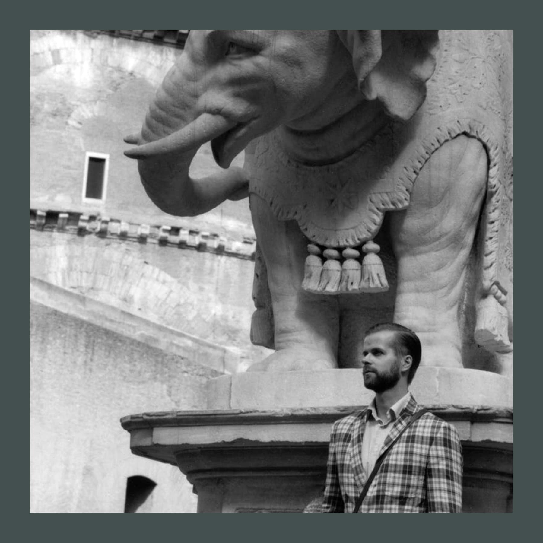 Black and white photograph of Max Renneisen in a checked jacket standing beneath Bernini's marble elephant in Rome
