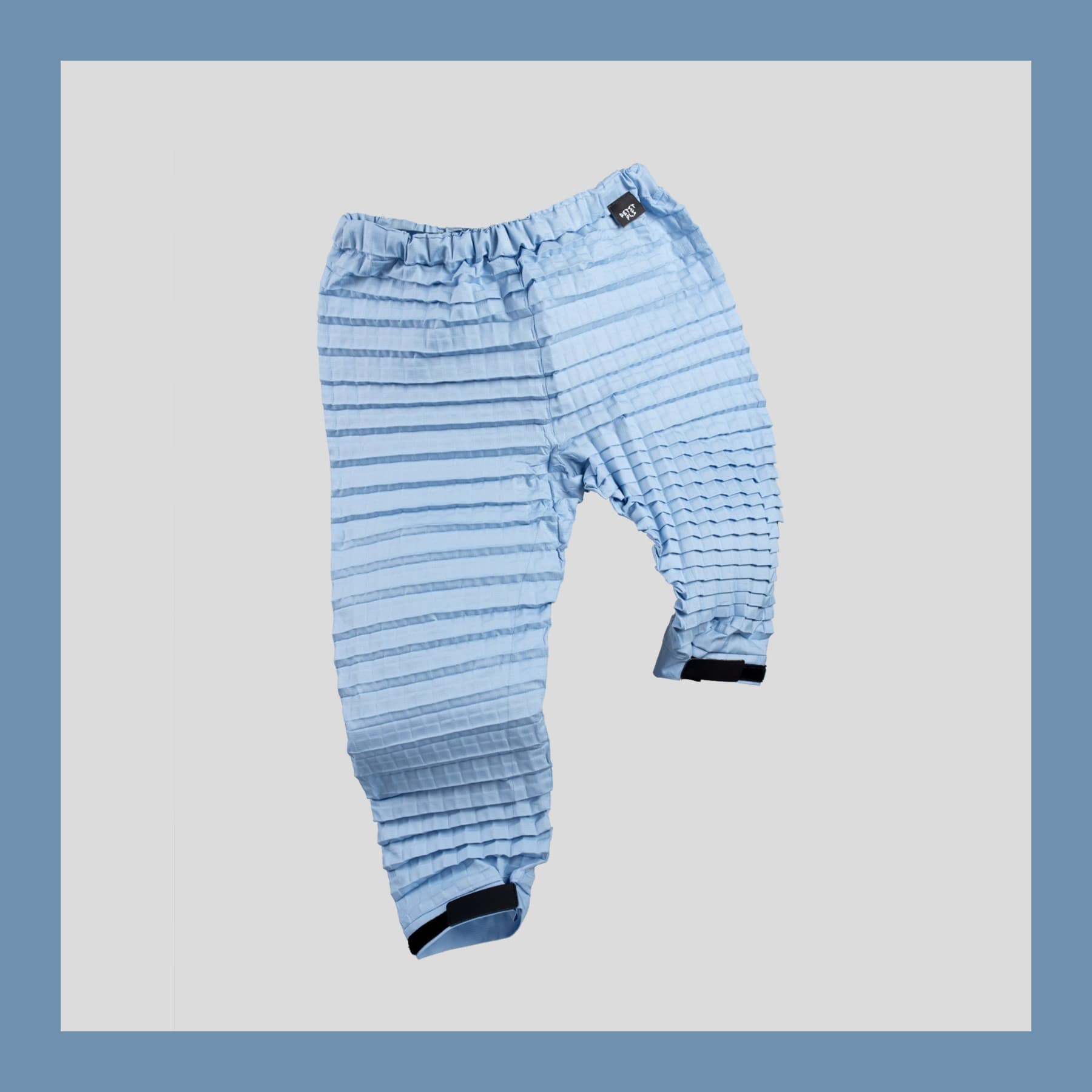 Petit Pli Versatile Bottoms in pale Polar Blue pleated ripstop on a grey background