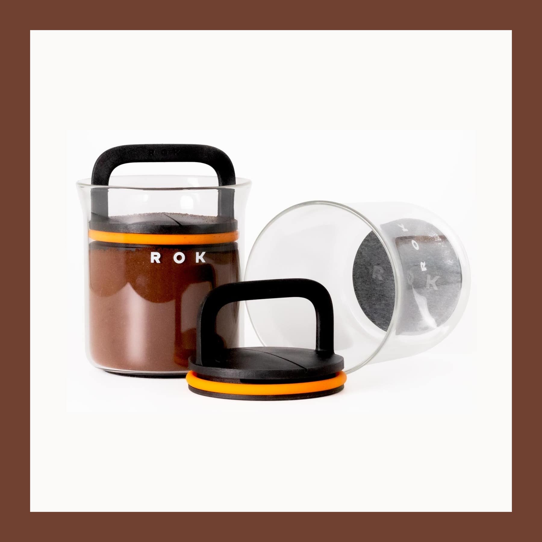 Two ROK Zero Jar glass jars with black plunger lids, one full of ground coffee and one lying open on its side
