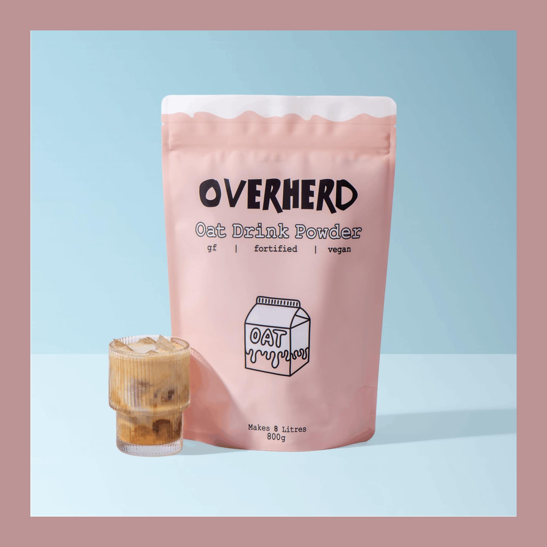 Pink 800g pouch of Overherd Oat Milk Powder beside an iced coffee on a pale blue background