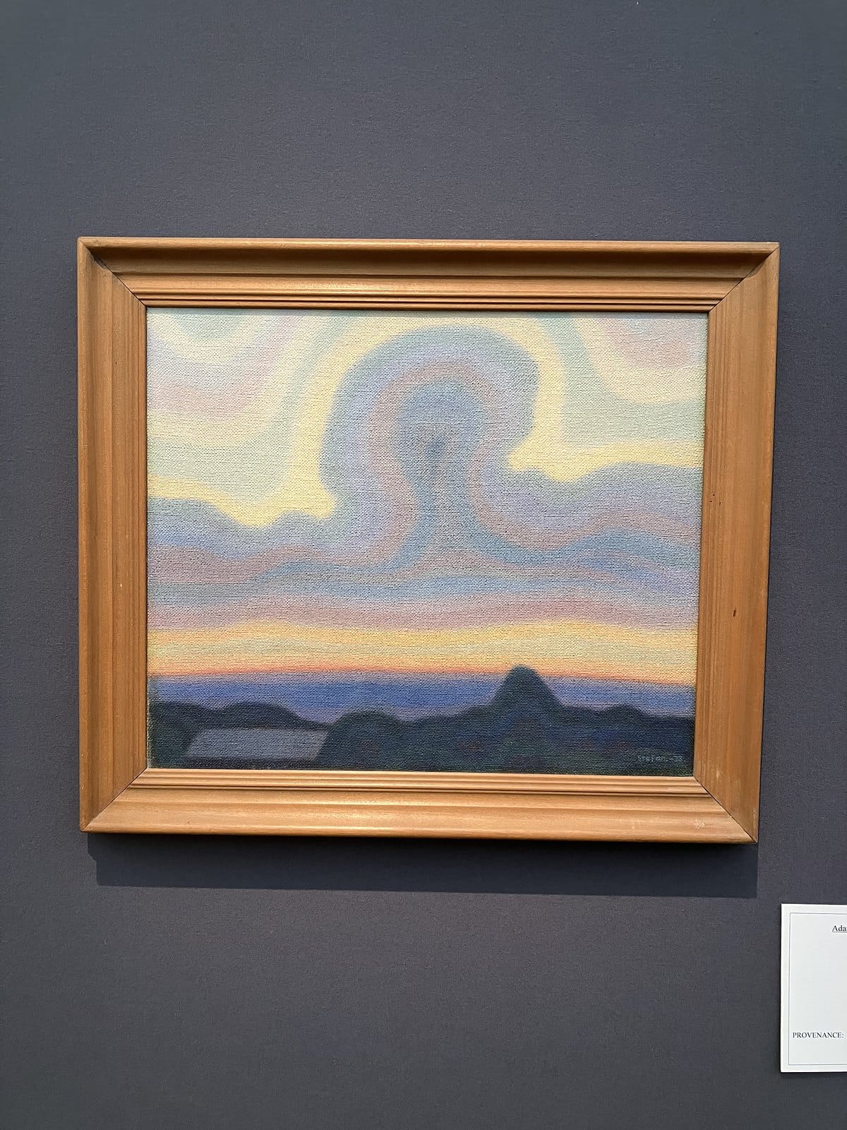 Stefan Johansson's small painting of swirling pastel clouds over a dark hilly horizon, in a pale wood frame