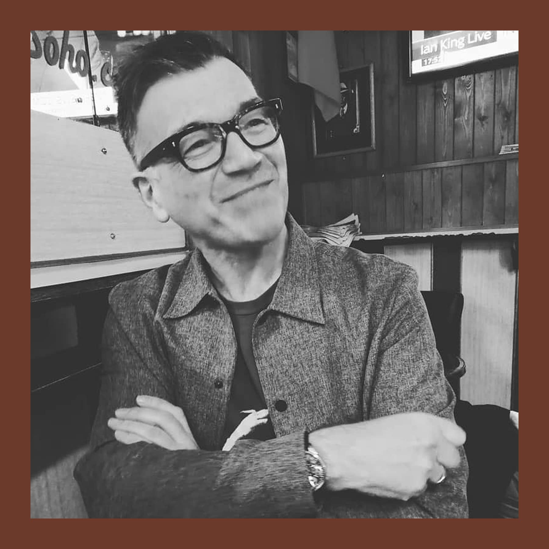 Black and white photograph of Andrew Torr in glasses and a grey jacket, arms folded, smiling in a wood-panelled pub