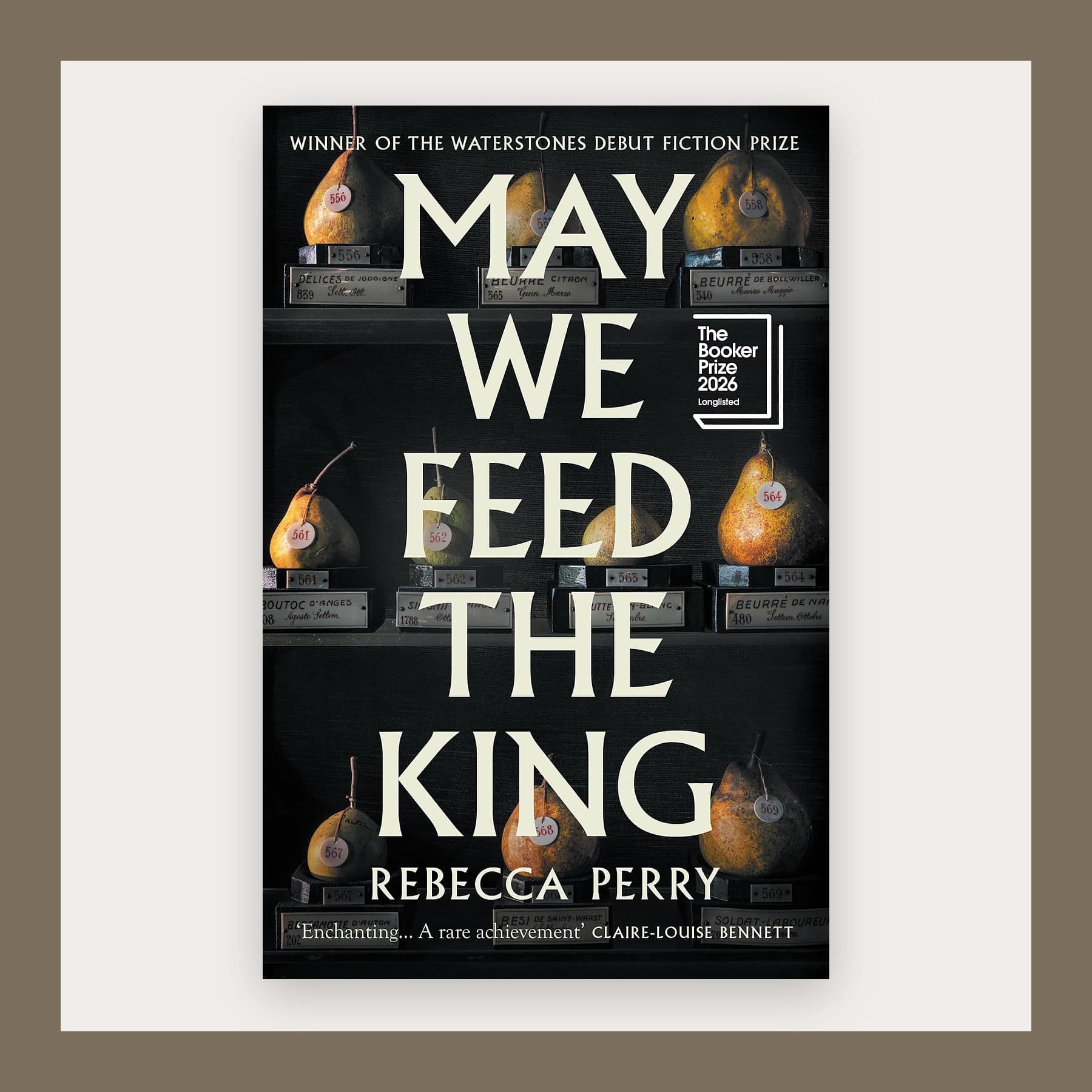 Black cover of May We Feed the King with pears in glass cases, in a taupe frame