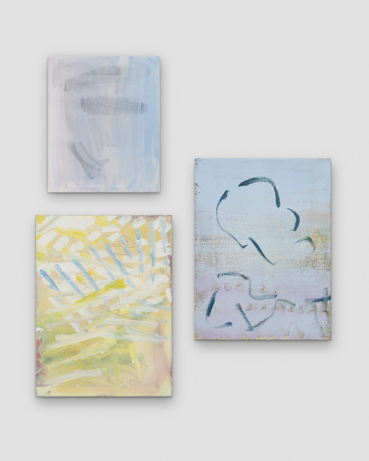 Three small abstract paintings by Daniel Pettitt hung as a group, with pale blue, lilac and yellow grounds and dark brushmarks