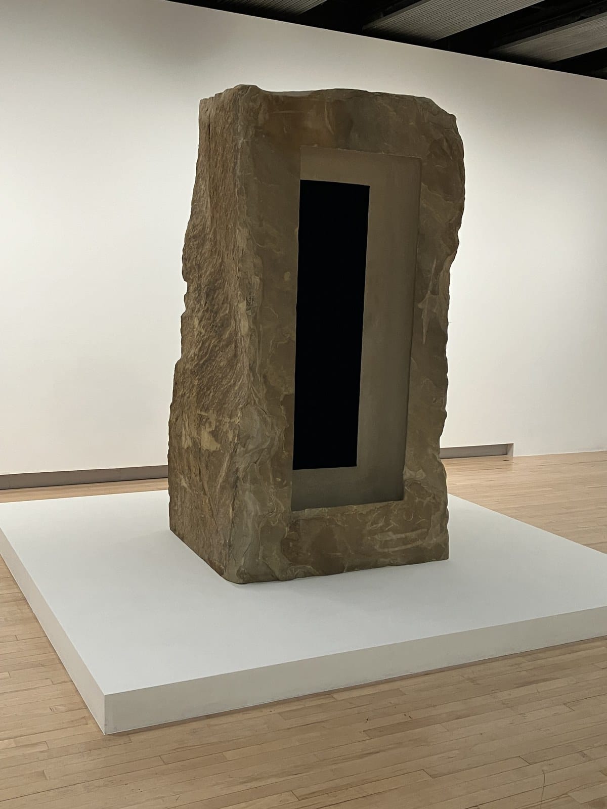 Rough sandstone block with a stepped doorway and a deep black inner rectangle, on a white plinth