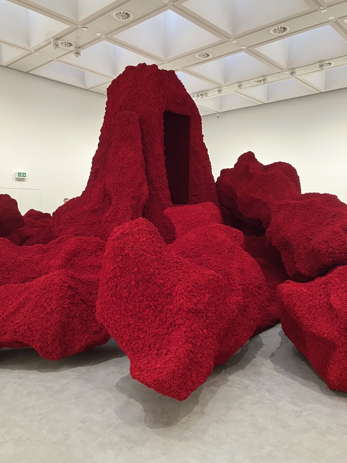 Large red pigment landscape with a dark doorway cut into its peak, by Anish Kapoor