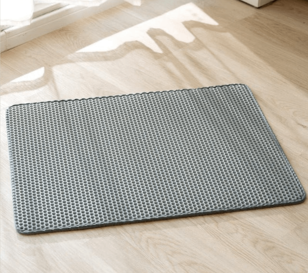 Grey textured cat litter mat on wooden floor, designed to trap litter from paws