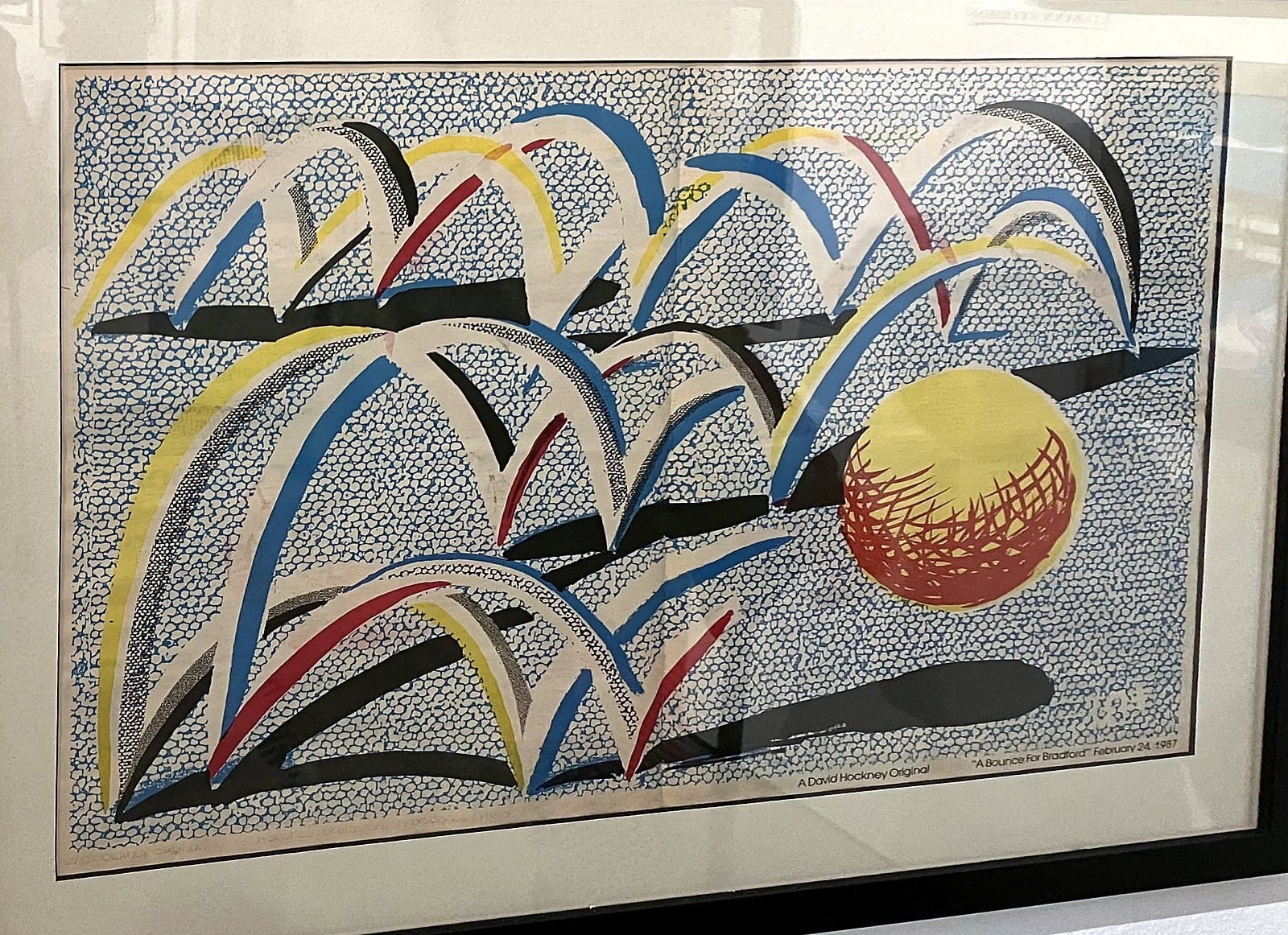 David Hockney print of red, yellow, blue and black arcs bouncing towards a yellow ball on a blue mesh