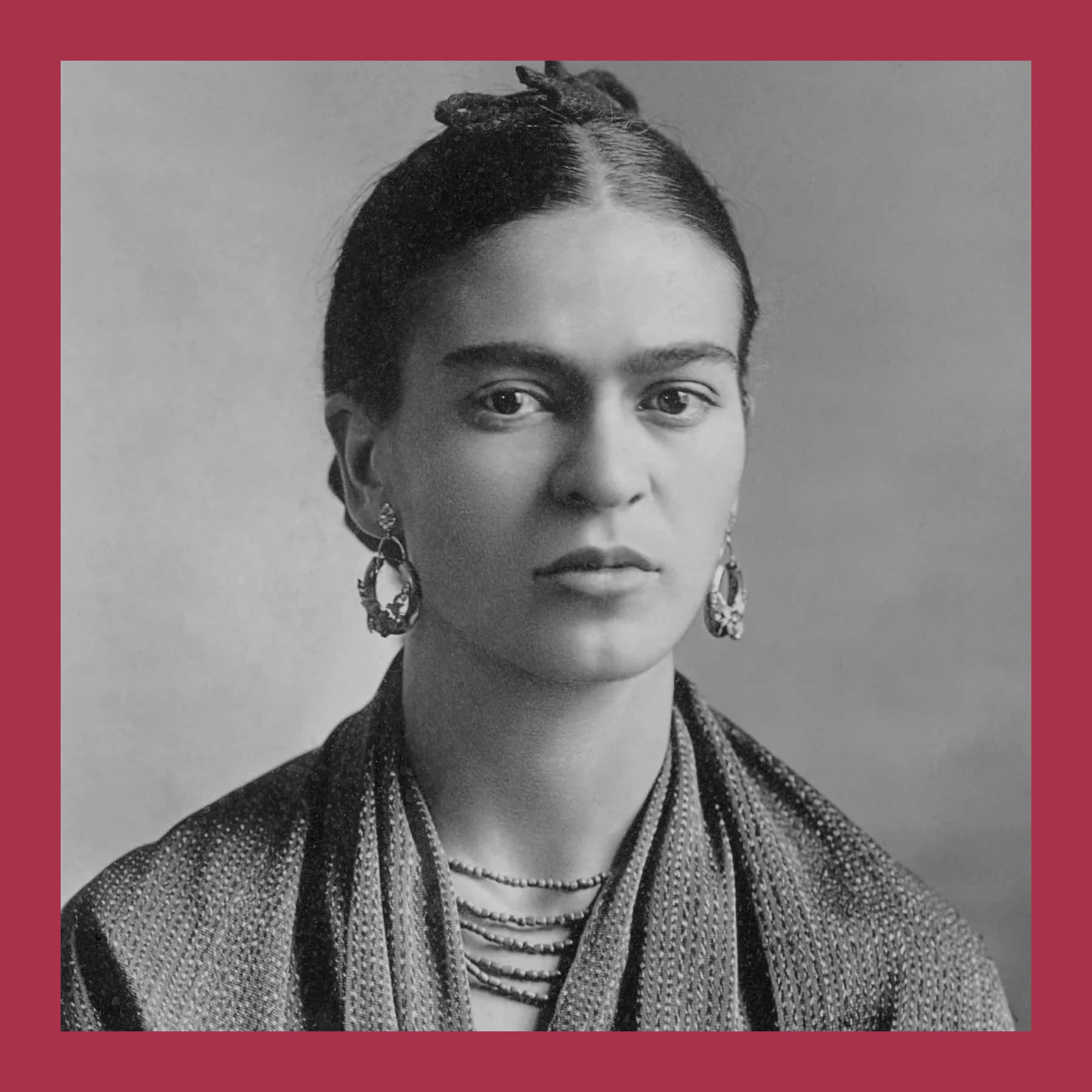 Black and white photograph of Frida Kahlo with her hair up, large earrings and a fringed shawl