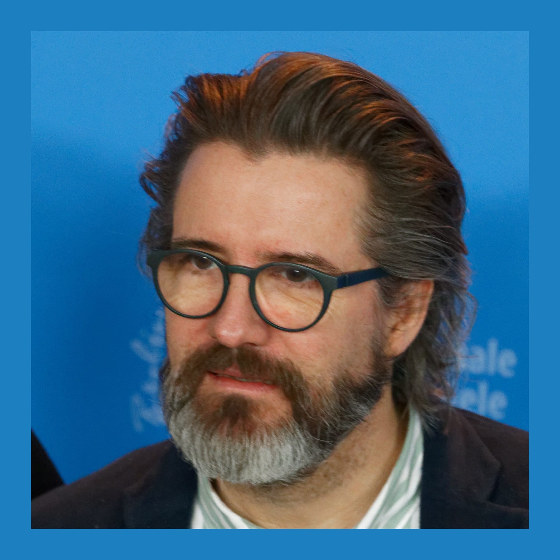 Olafur Eliasson with swept-back hair, round glasses and a grey beard, in a striped shirt and dark jacket