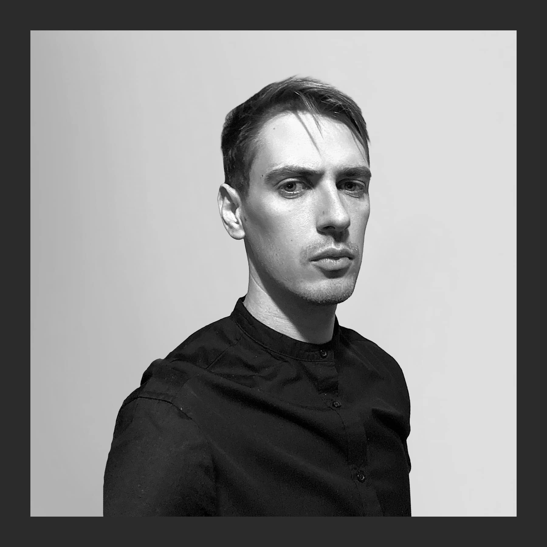 Black and white portrait of Rostislaw Tsarenko in a black band-collar shirt against a plain light background
