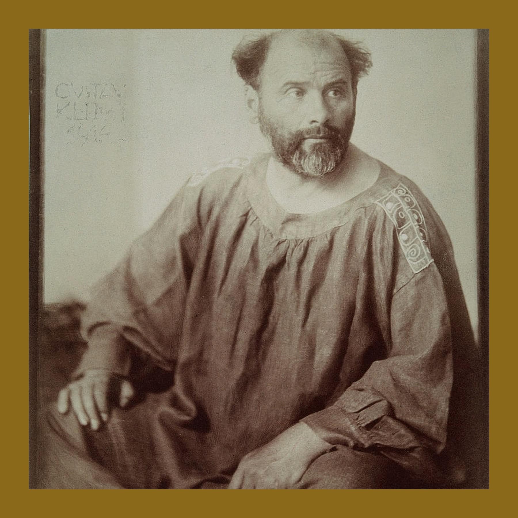Sepia photograph of Gustav Klimt with a beard, sitting in a long painter’s smock