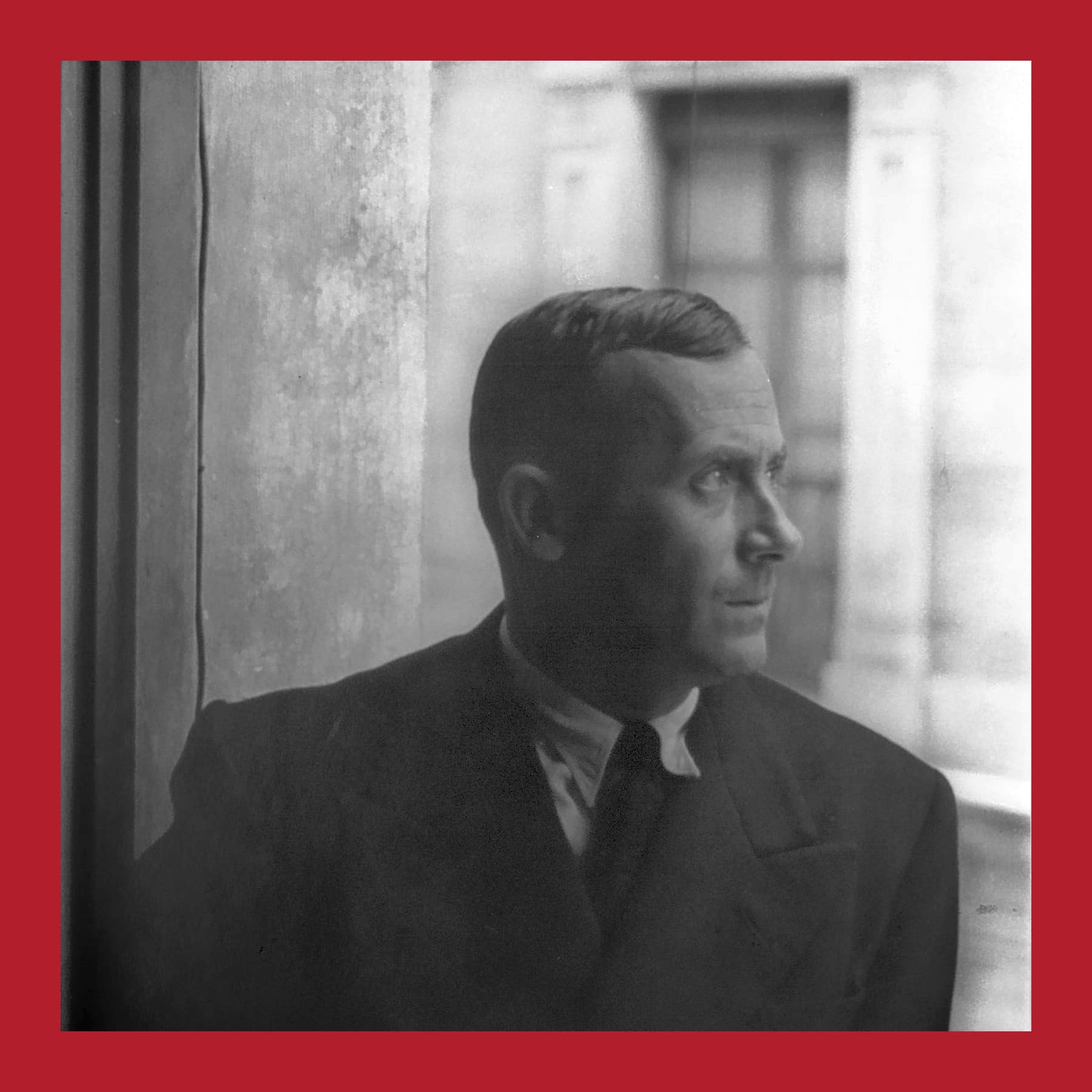 Black and white photograph of Joan Miró in a dark suit and tie, looking out of a window