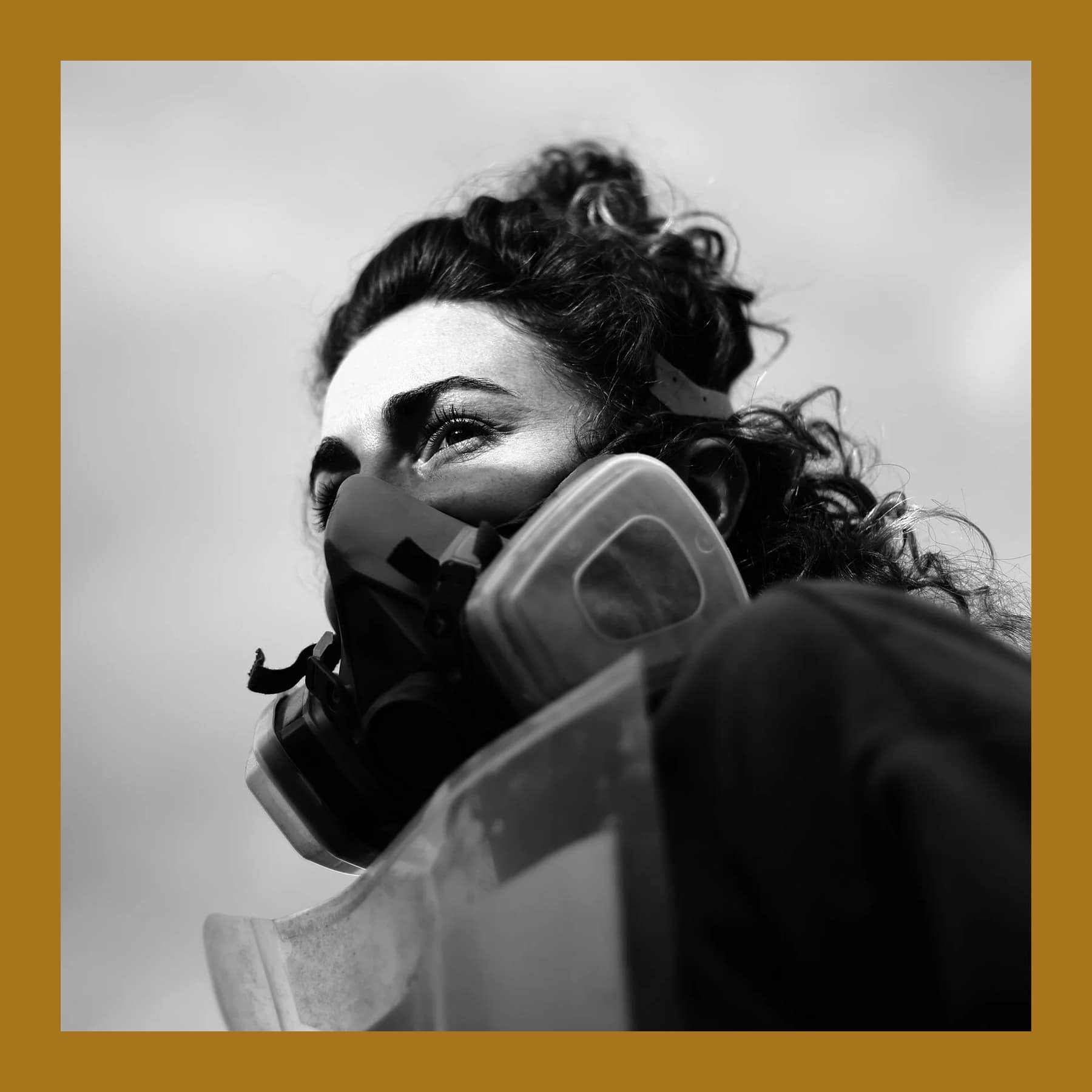 Black and white photo of Rosie Woods in profile wearing a spray-paint respirator mask against the sky