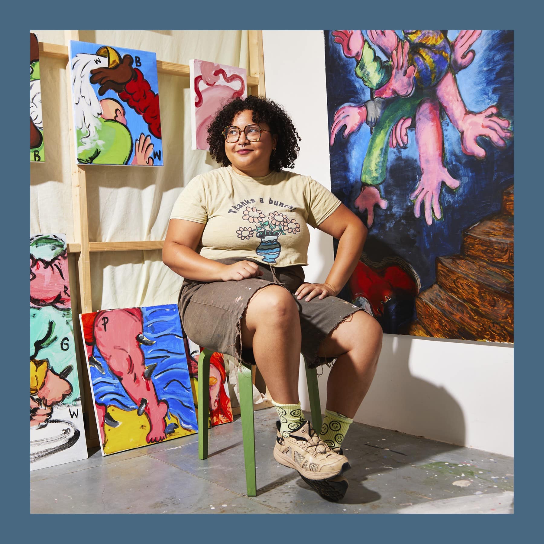 Olivia Sterling sitting on a green stool in her studio, surrounded by her paintings of hands and food