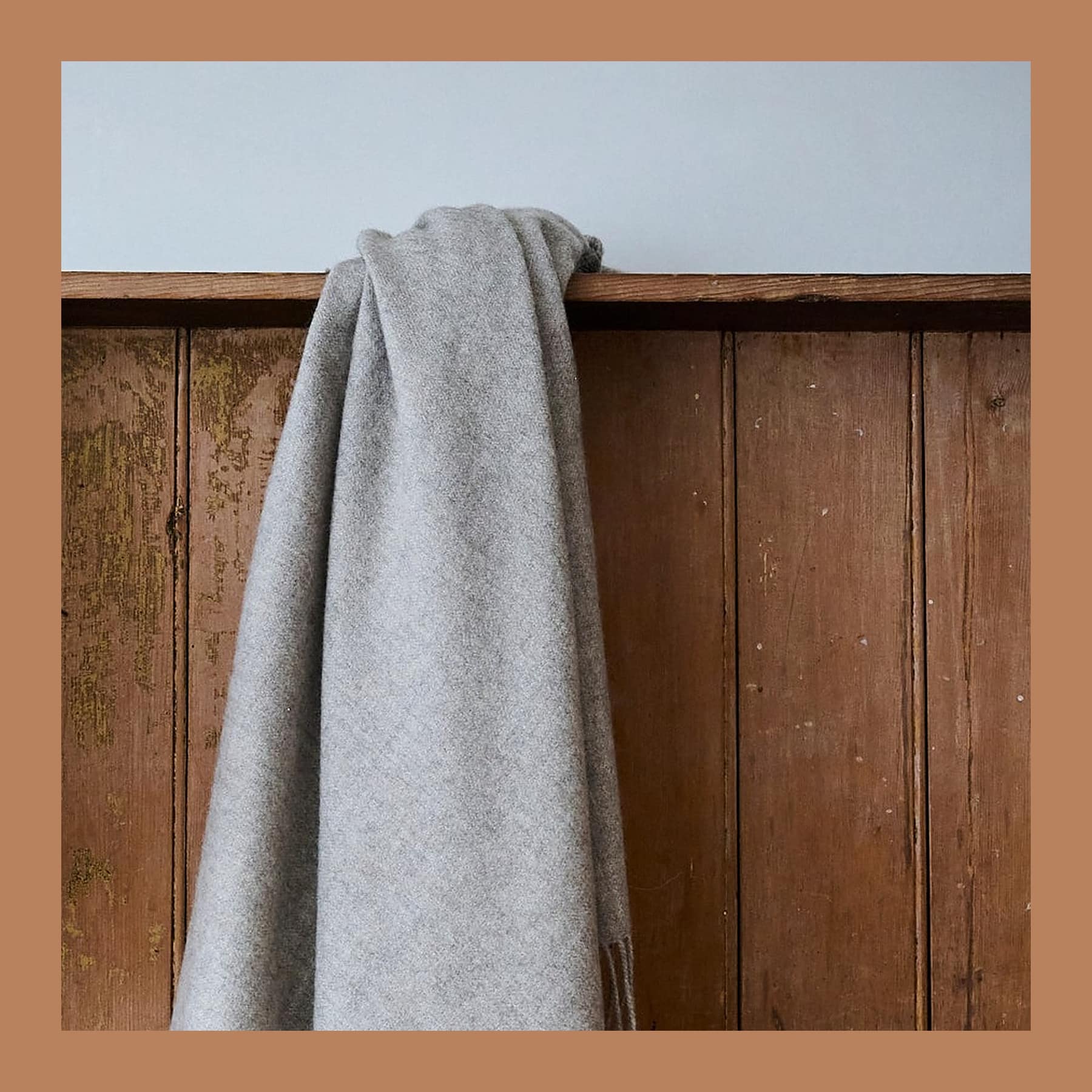 Plain grey undyed alpaca blanket with a thin dark selvedge stripe, hanging over the back of a pine settle.