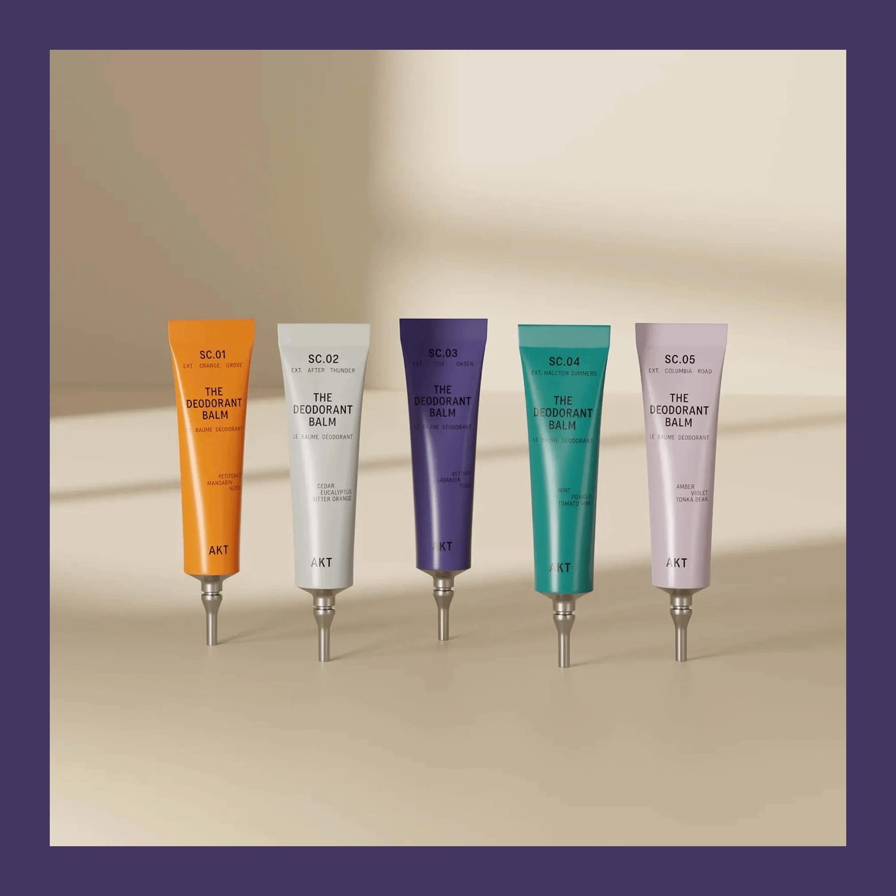 Five AKT London deodorant balm tubes in orange, white, purple, teal and lilac standing in a row