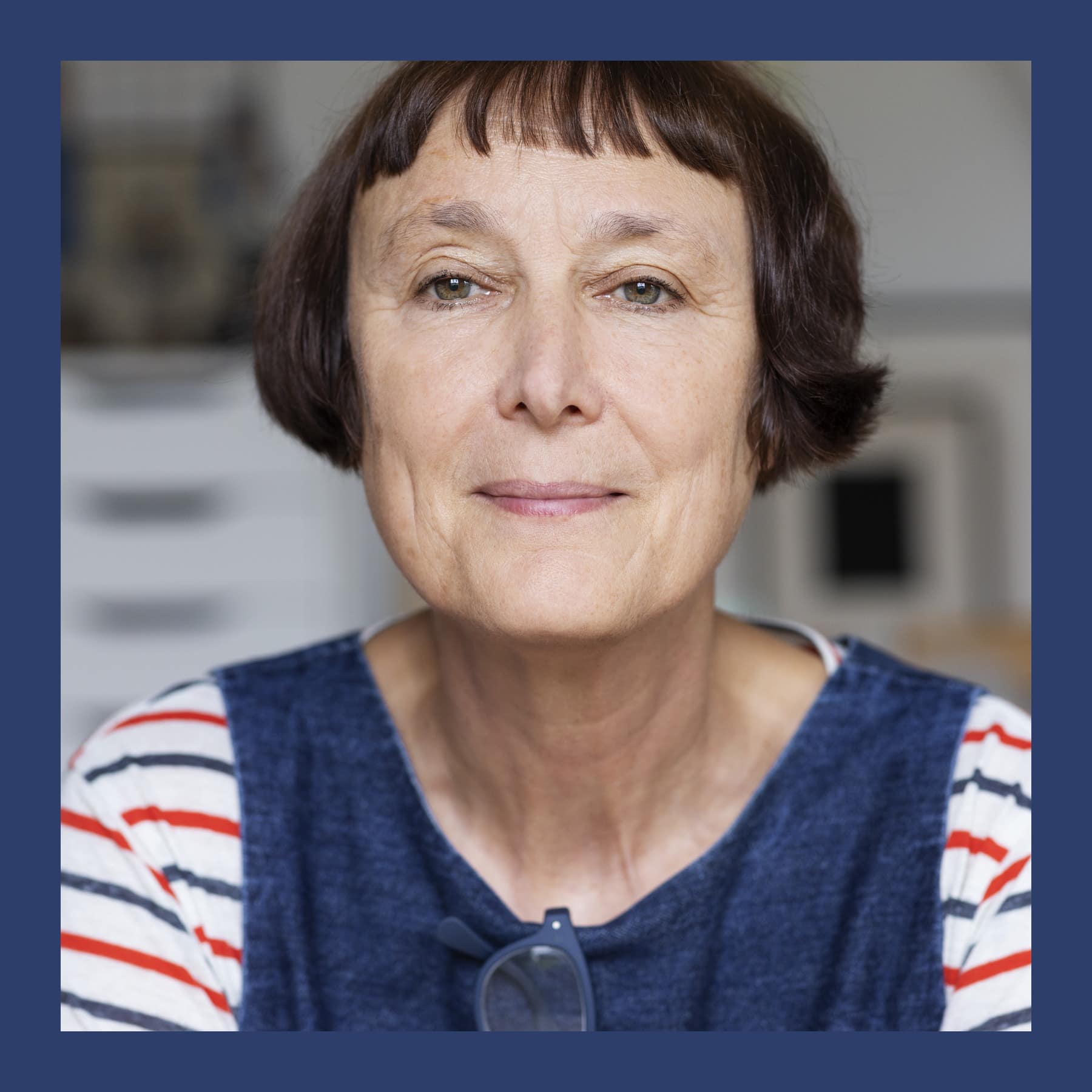 Cornelia Parker with a dark fringe, in a striped top and blue pinafore, in her studio