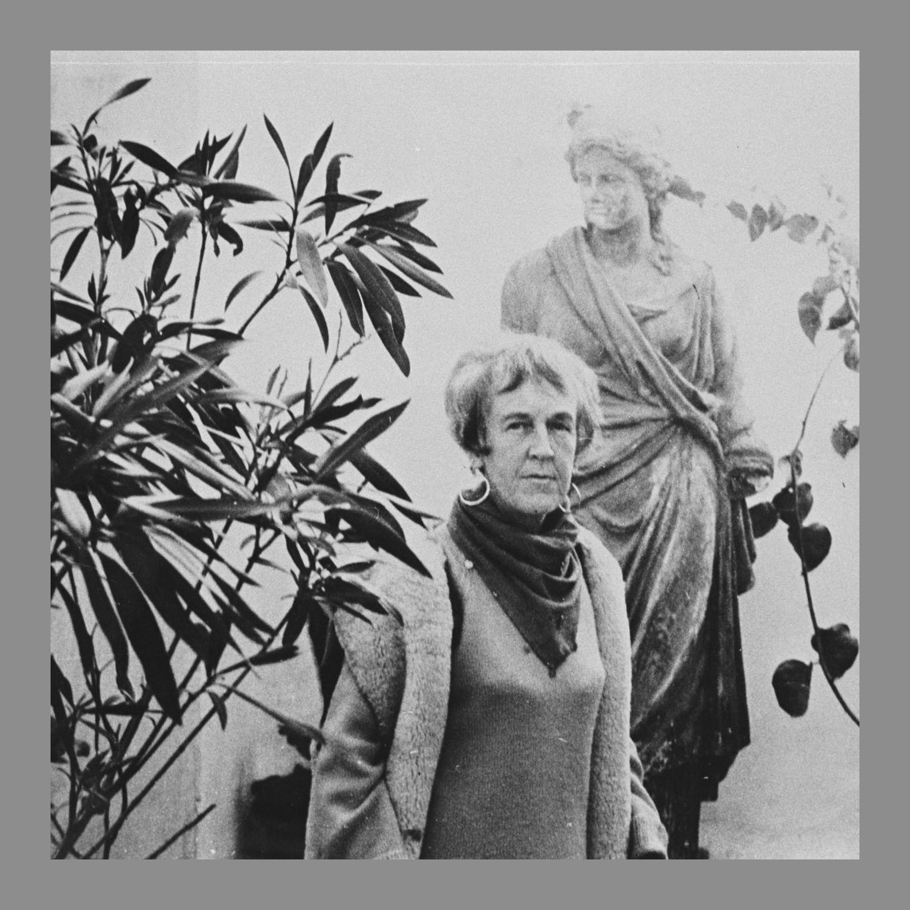 Black and white photo of Barbara Hepworth in a scarf beside a classical statue
