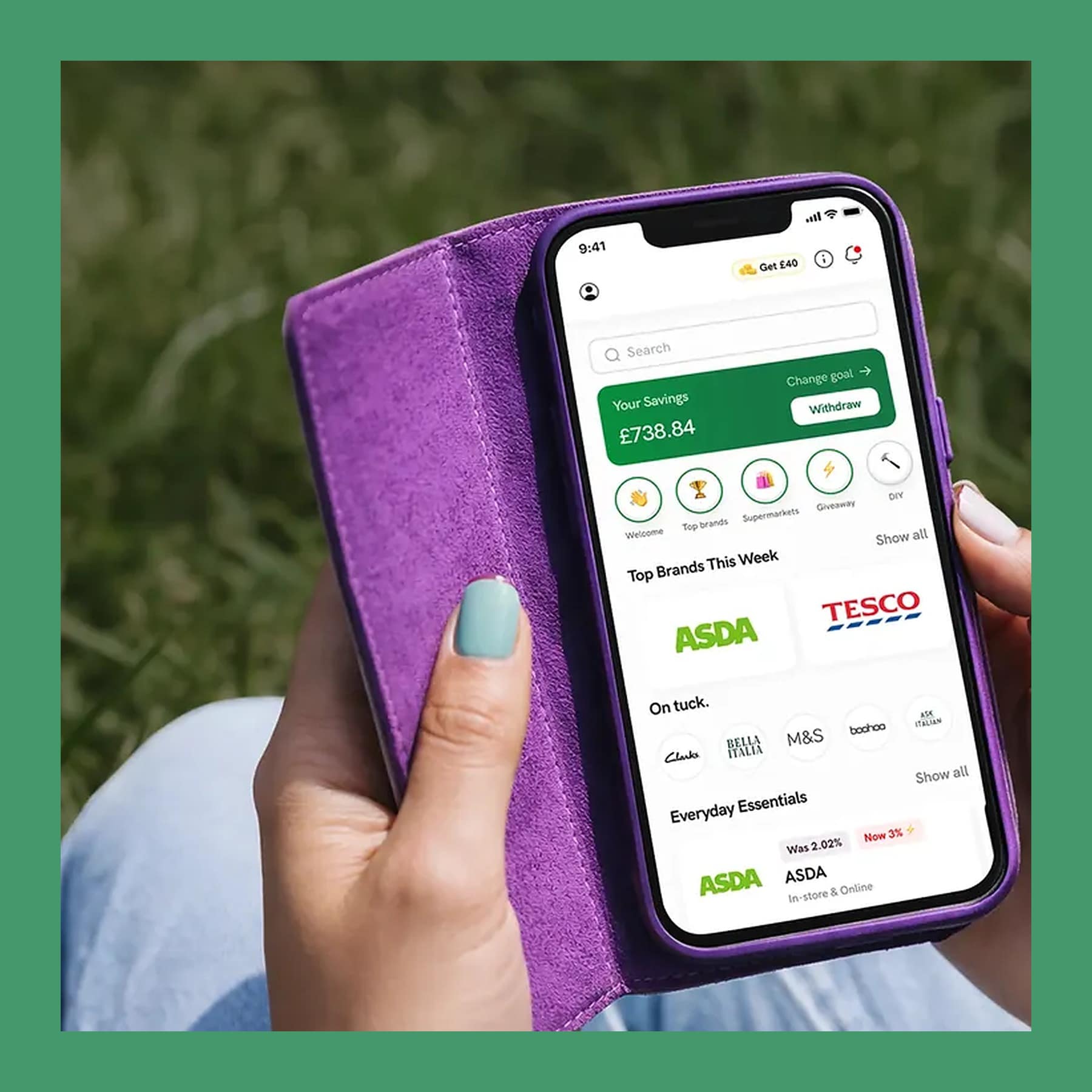 Hand holding a phone in a purple case showing the tuck. cashback app home screen with ASDA and Tesco