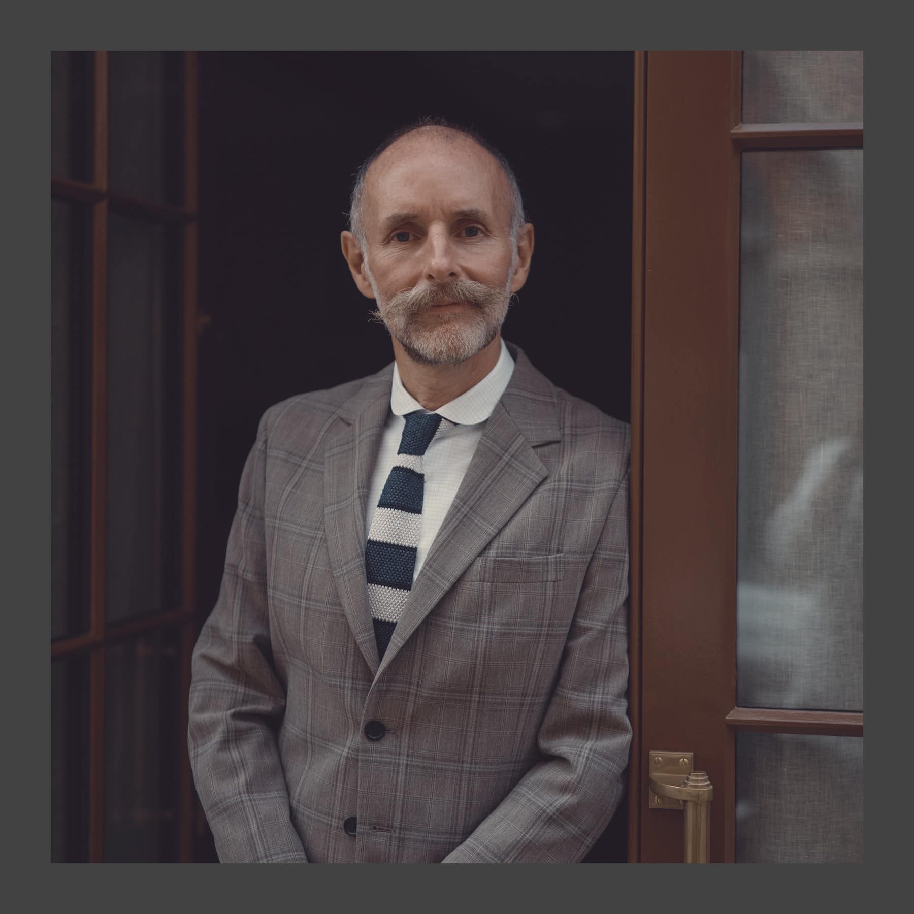 Glenn Brown in a checked suit and striped tie standing in a doorway