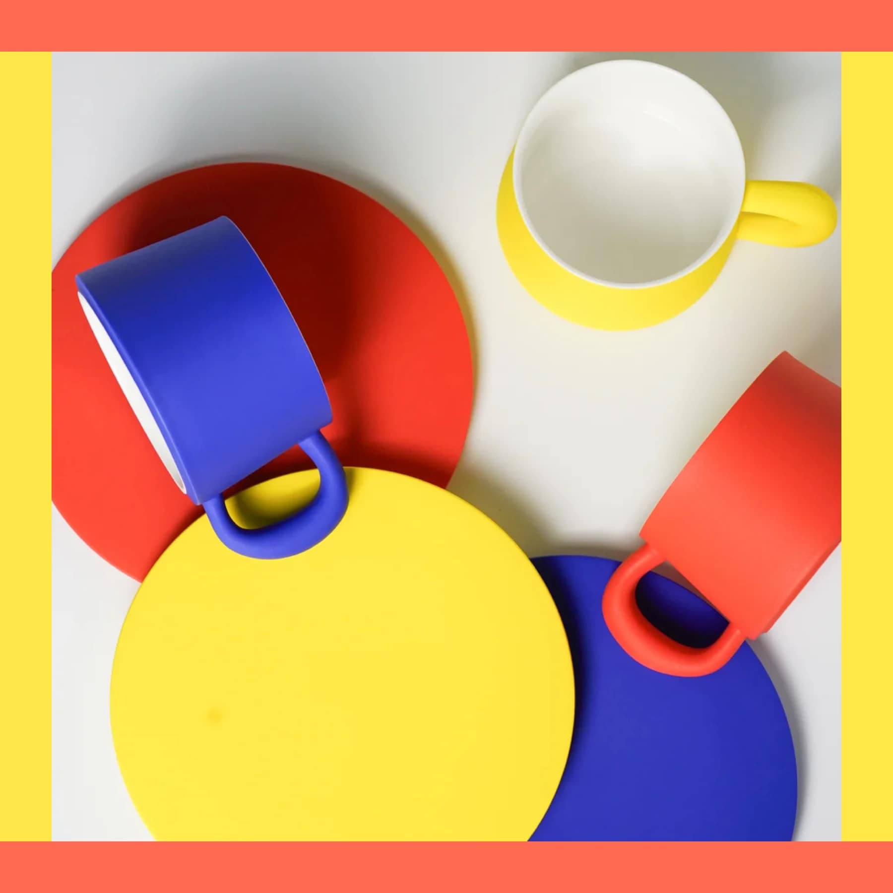 Overhead view of Hazzey Studio Prime Colours mugs and cups in bright blue, red, and yellow, arranged on matching circular plates.