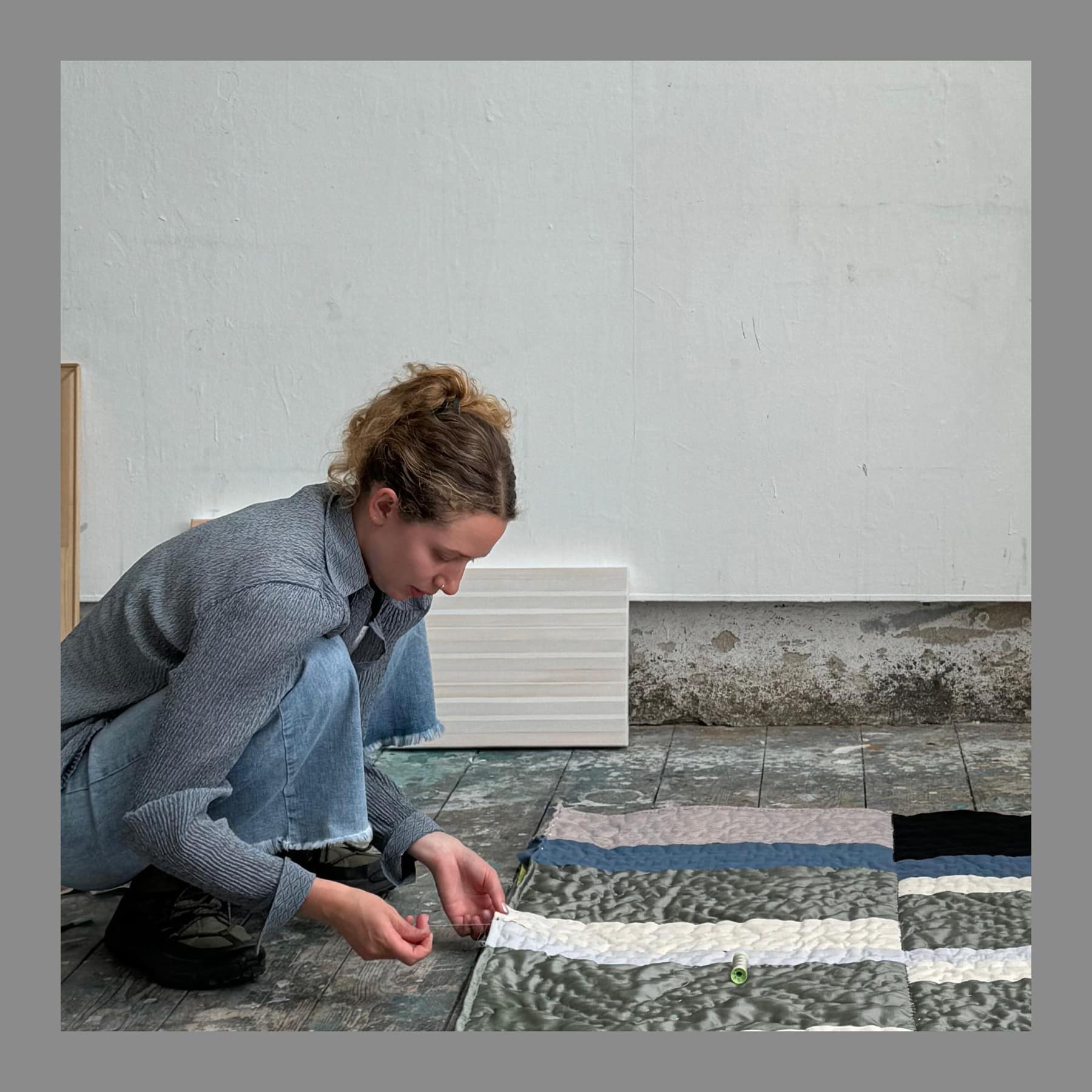 Raphaella Pester kneeling on her studio floor working on a striped textile piece