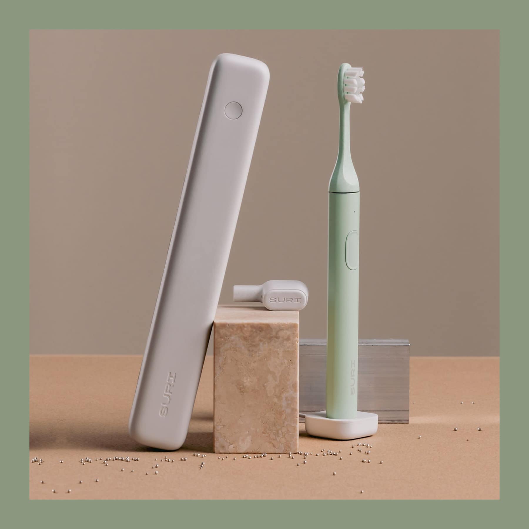 SURI Pro 2.0 electric toothbrush in sage green beside its grey UV-C travel case on a stone block