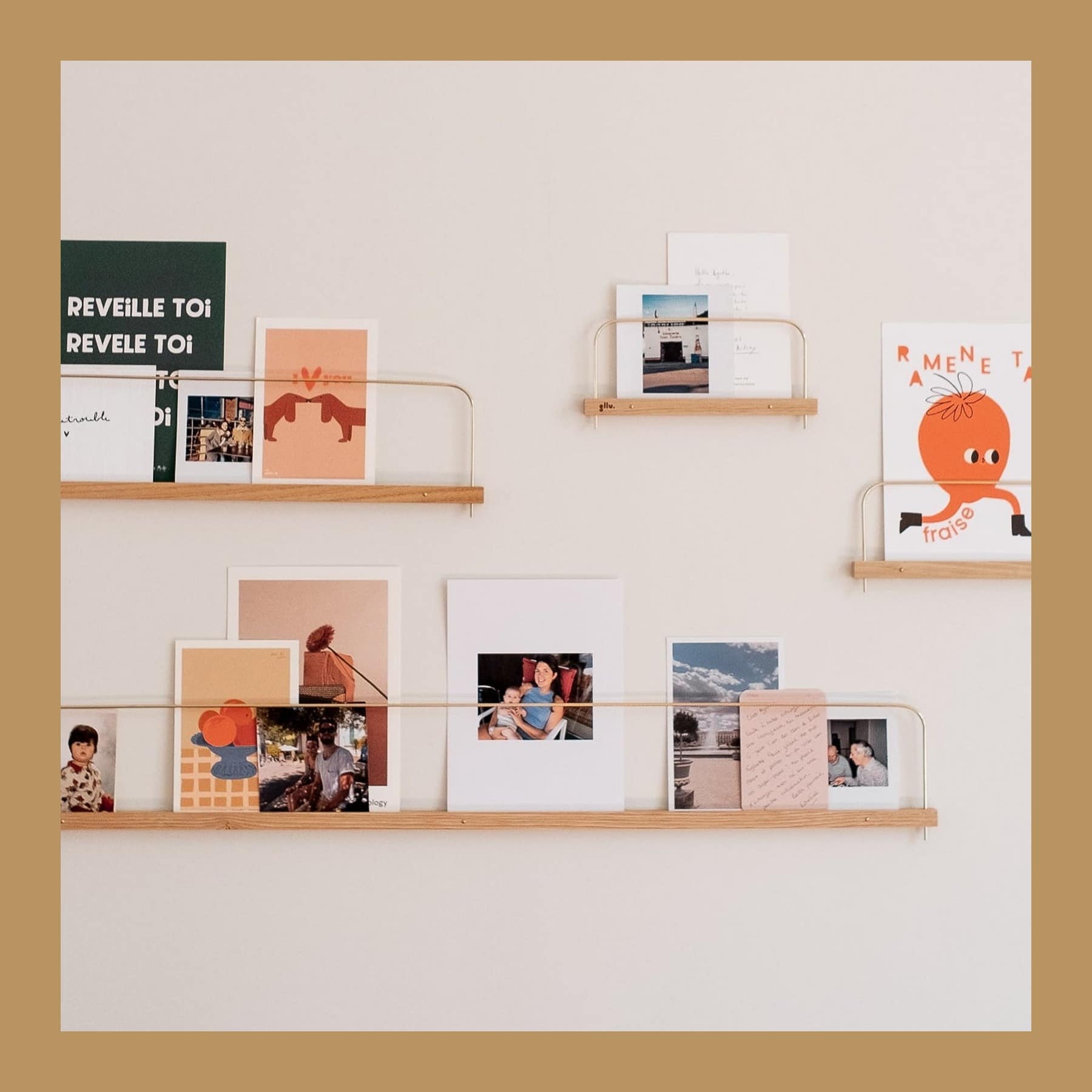 Two Gllu Super-Poses chestnut and brass shelves on a wall holding postcards and photos