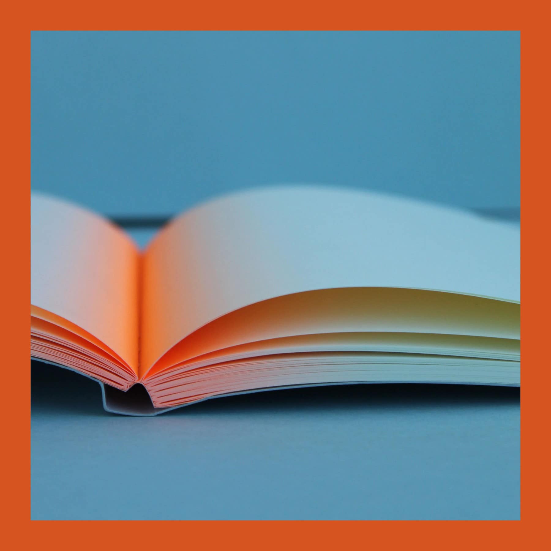 The Mark+Fold Glow notebook open on a blue surface, with a neon orange gradient glowing from the centre fold