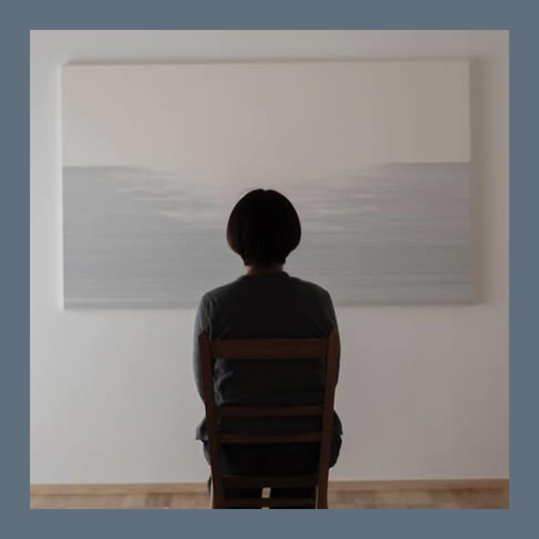 Shunshun seen from behind, seated on a wooden chair in front of one of his large pale grey paintings