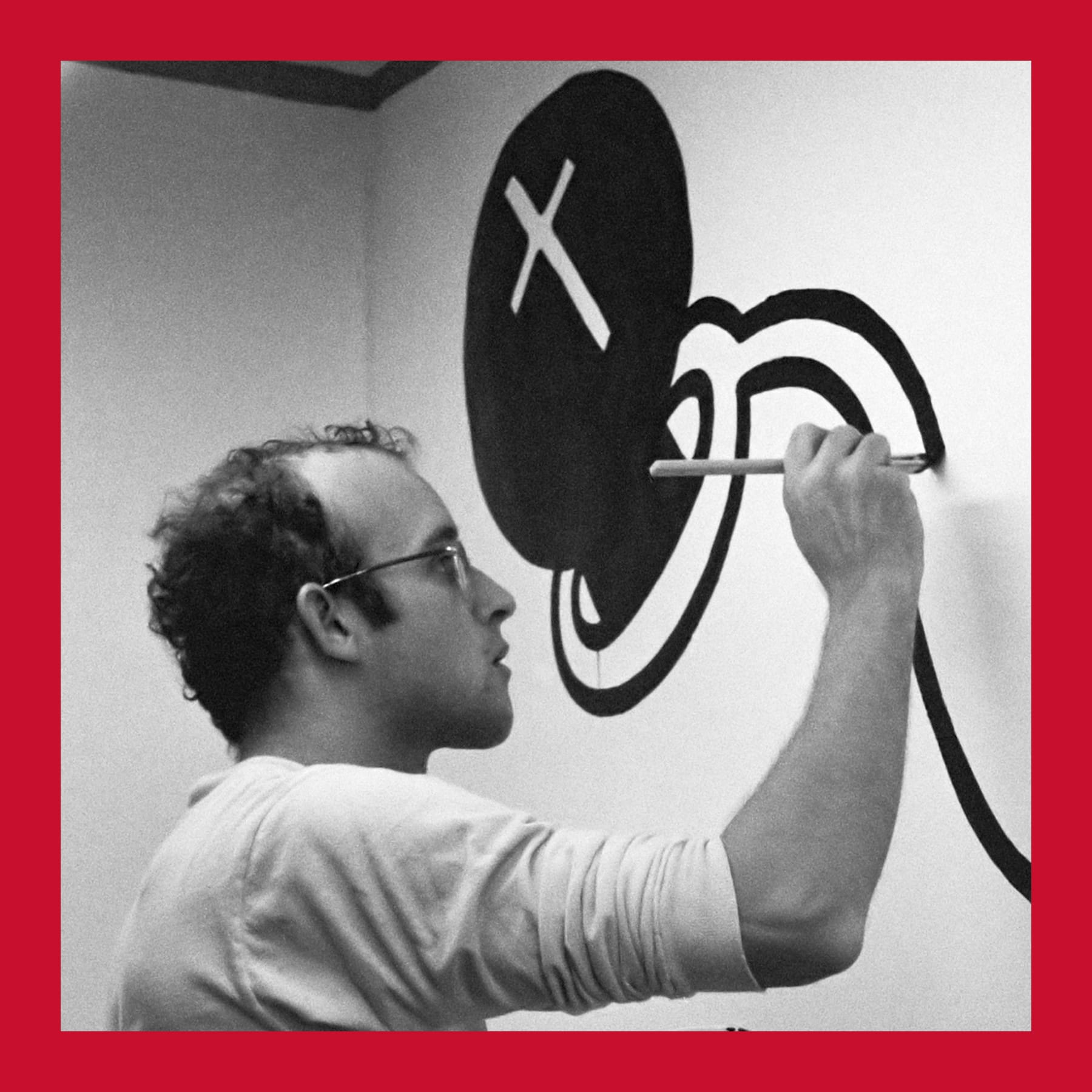 Keith Haring painting a large black and white drawing on a gallery wall