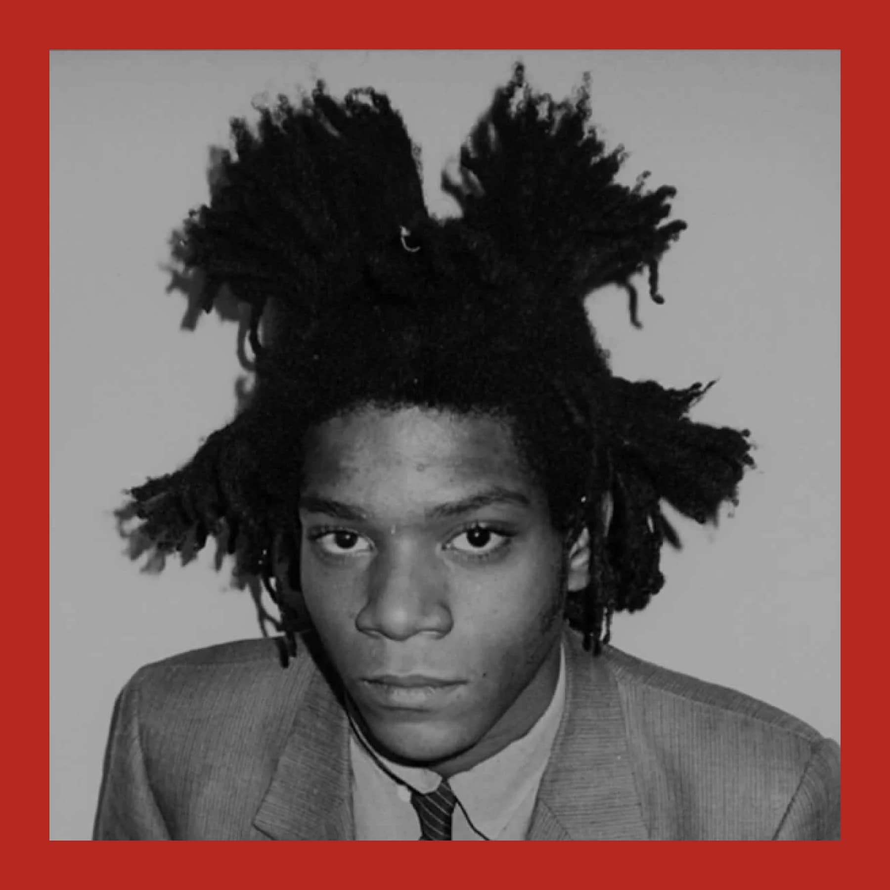 Black and white portrait of Jean-Michel Basquiat in a suit and striped tie, his hair in upright dreadlocks