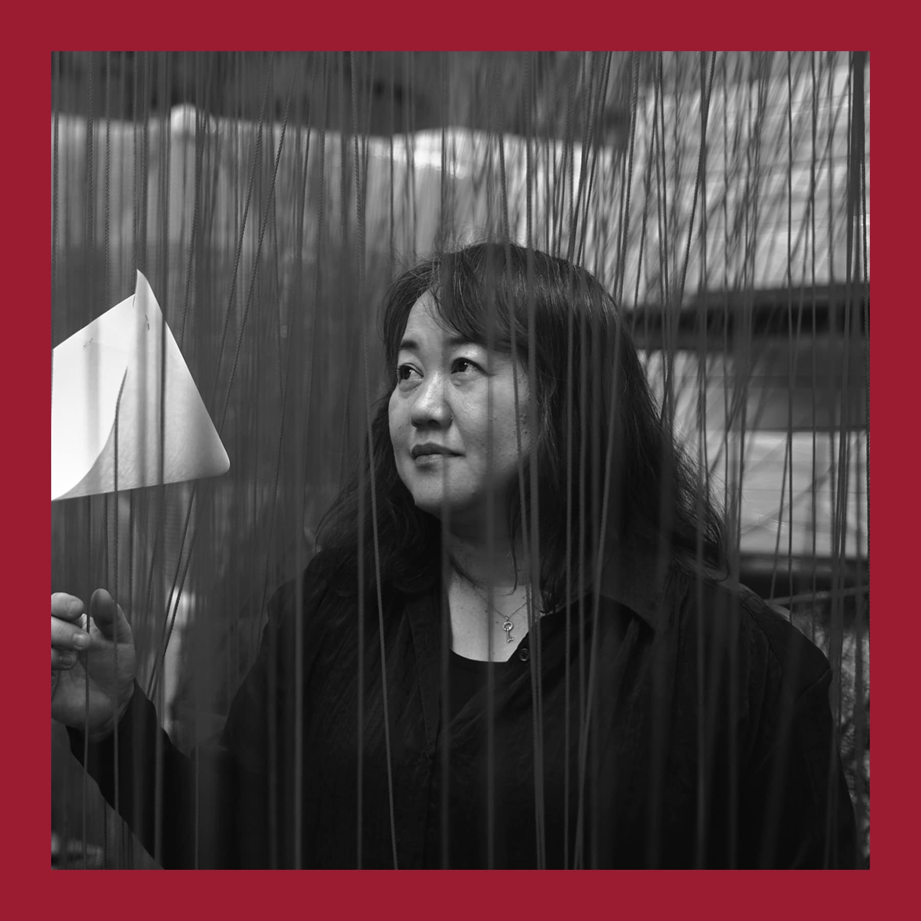 Chiharu Shiota in black, looking up among hanging threads in her studio