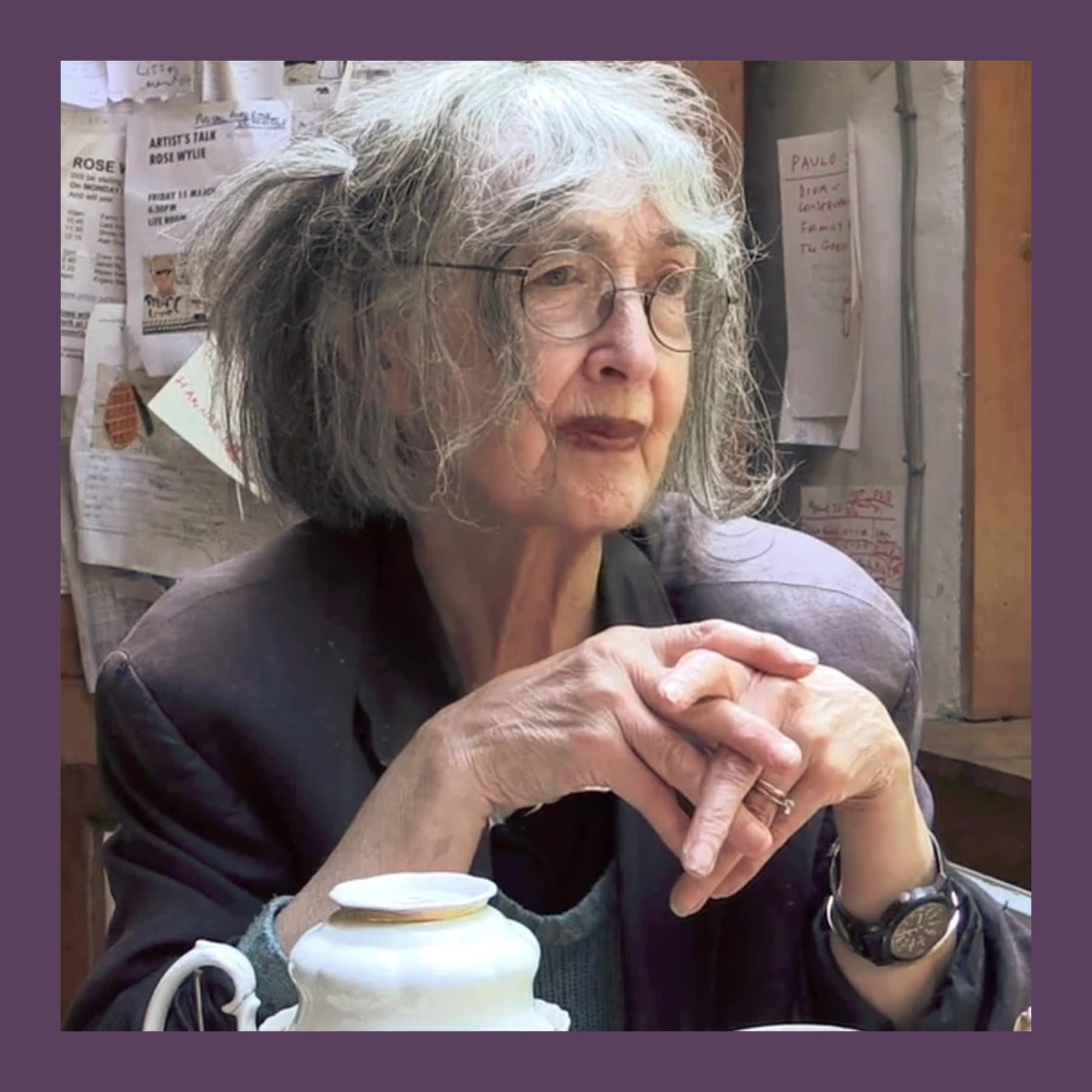 Rose Wylie in her Kent studio in 2014, hands clasped, with notes pinned to the wall behind her