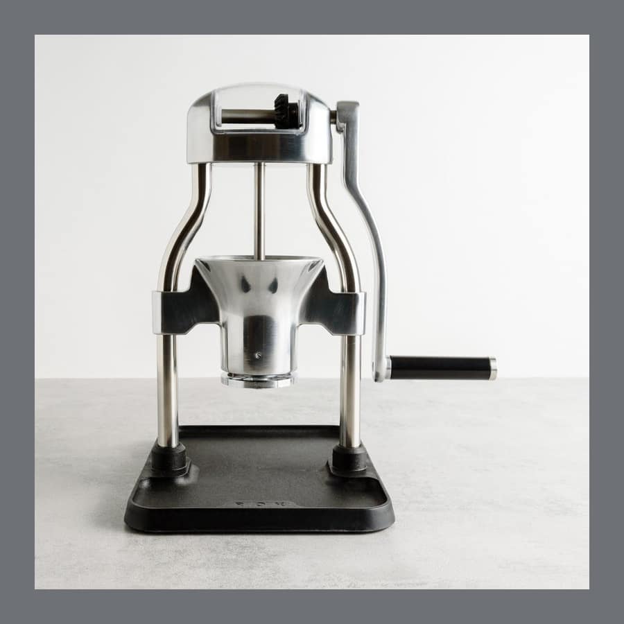 ROK GrinderGC hand coffee grinder in polished aluminium with a long lever arm, on a grey worktop