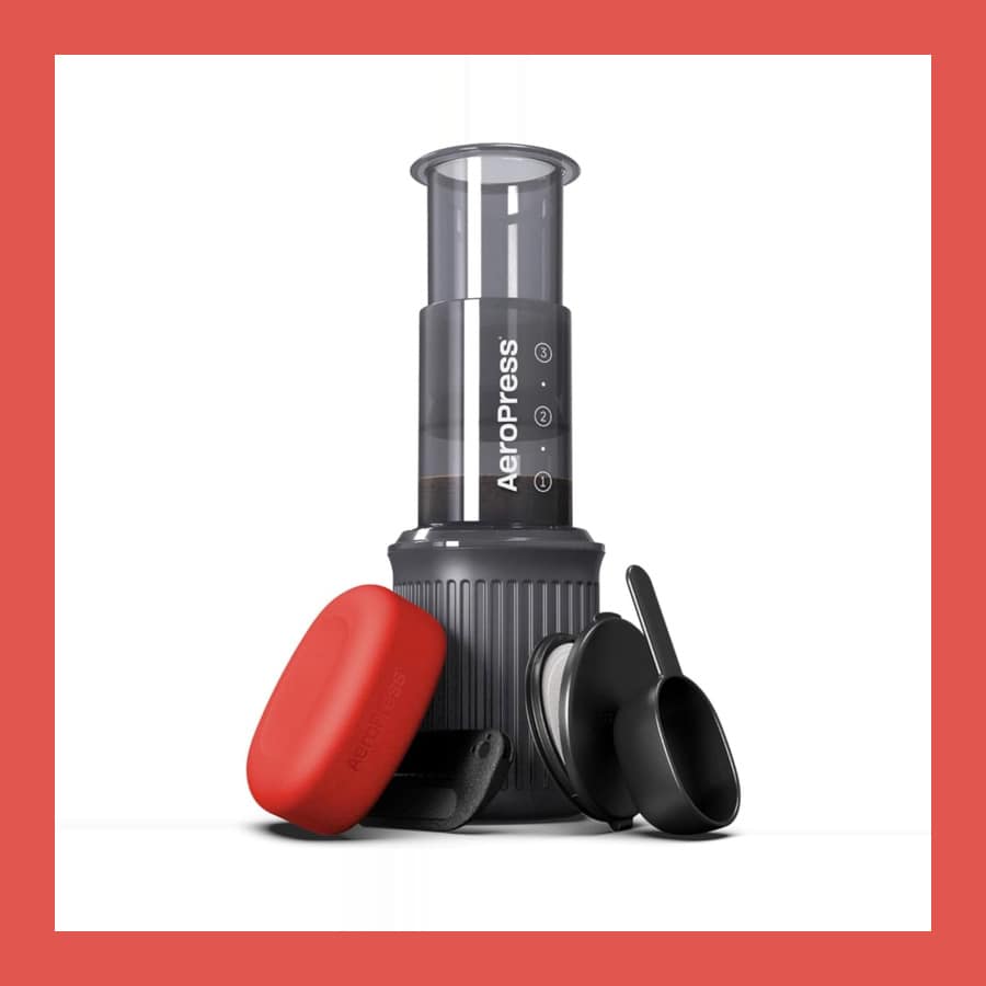 AeroPress Go travel coffee press in grey with its red silicone mug lid and black stirrer and scoop