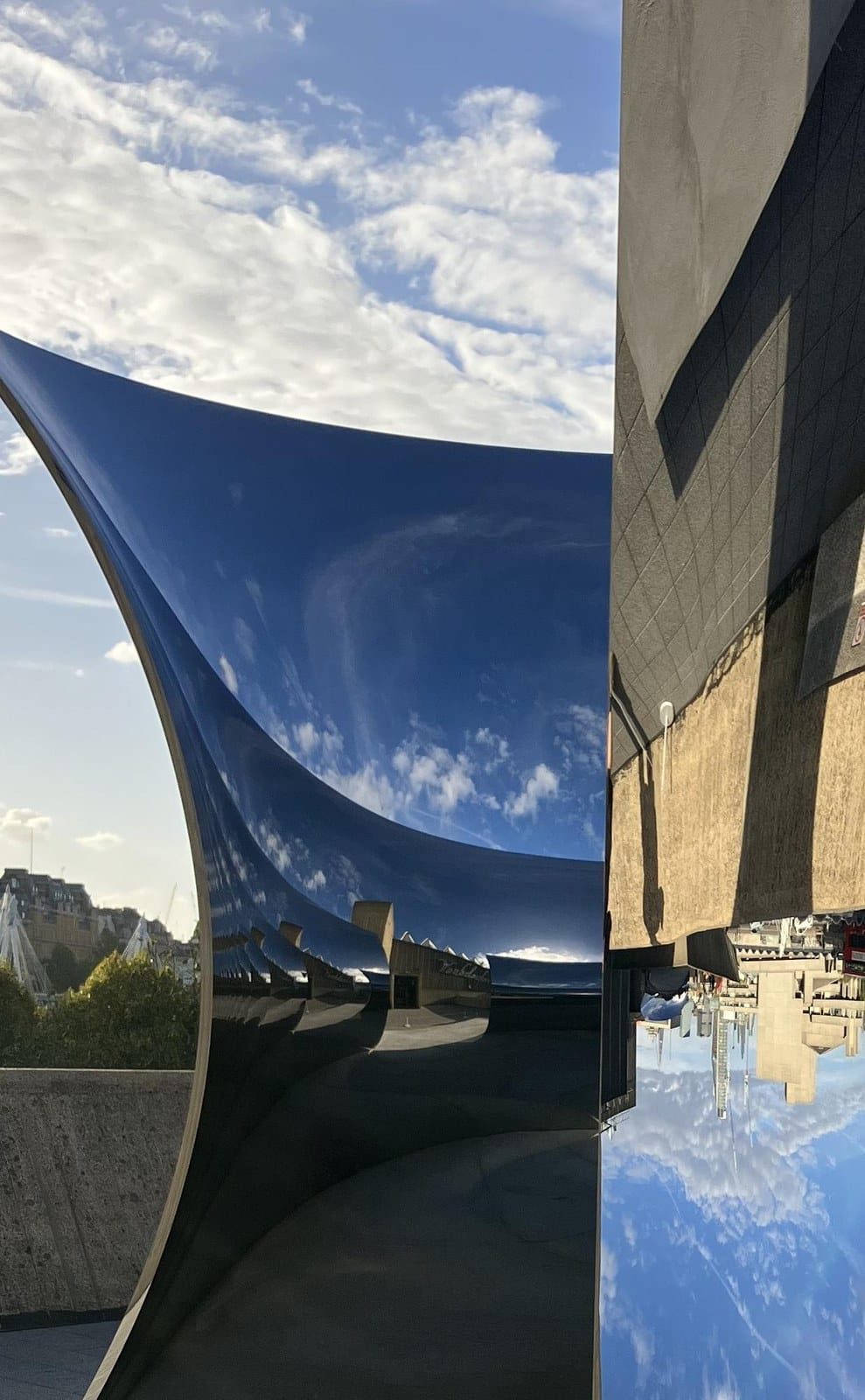 Curved polished steel sculpture reflecting blue sky and the Southbank upside down