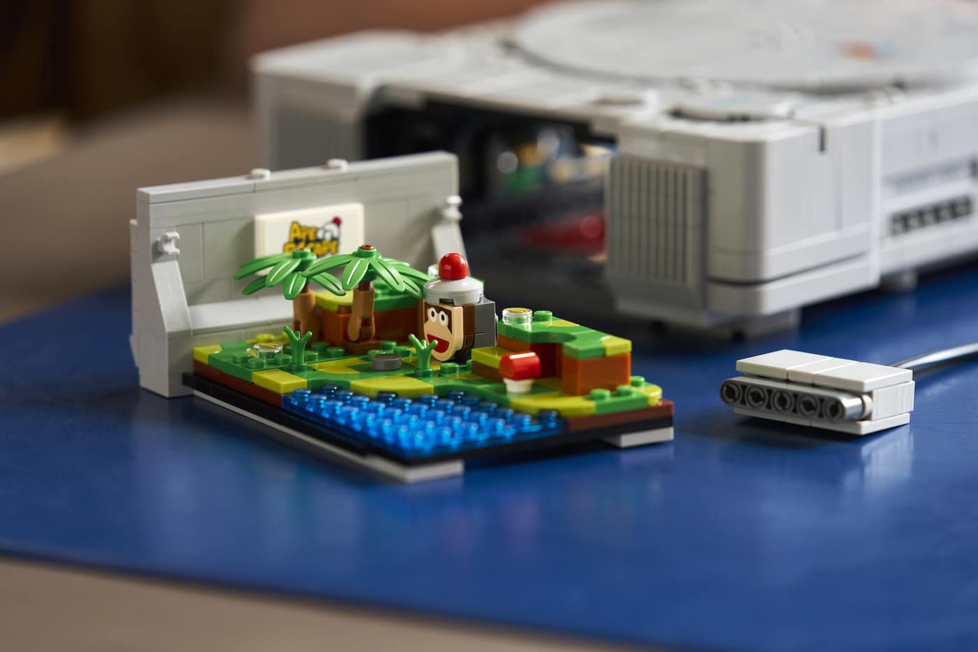 Brick-built Ape Escape diorama pulled out of the LEGO PlayStation console, with a monkey figure on a green island and a brick memory card beside it