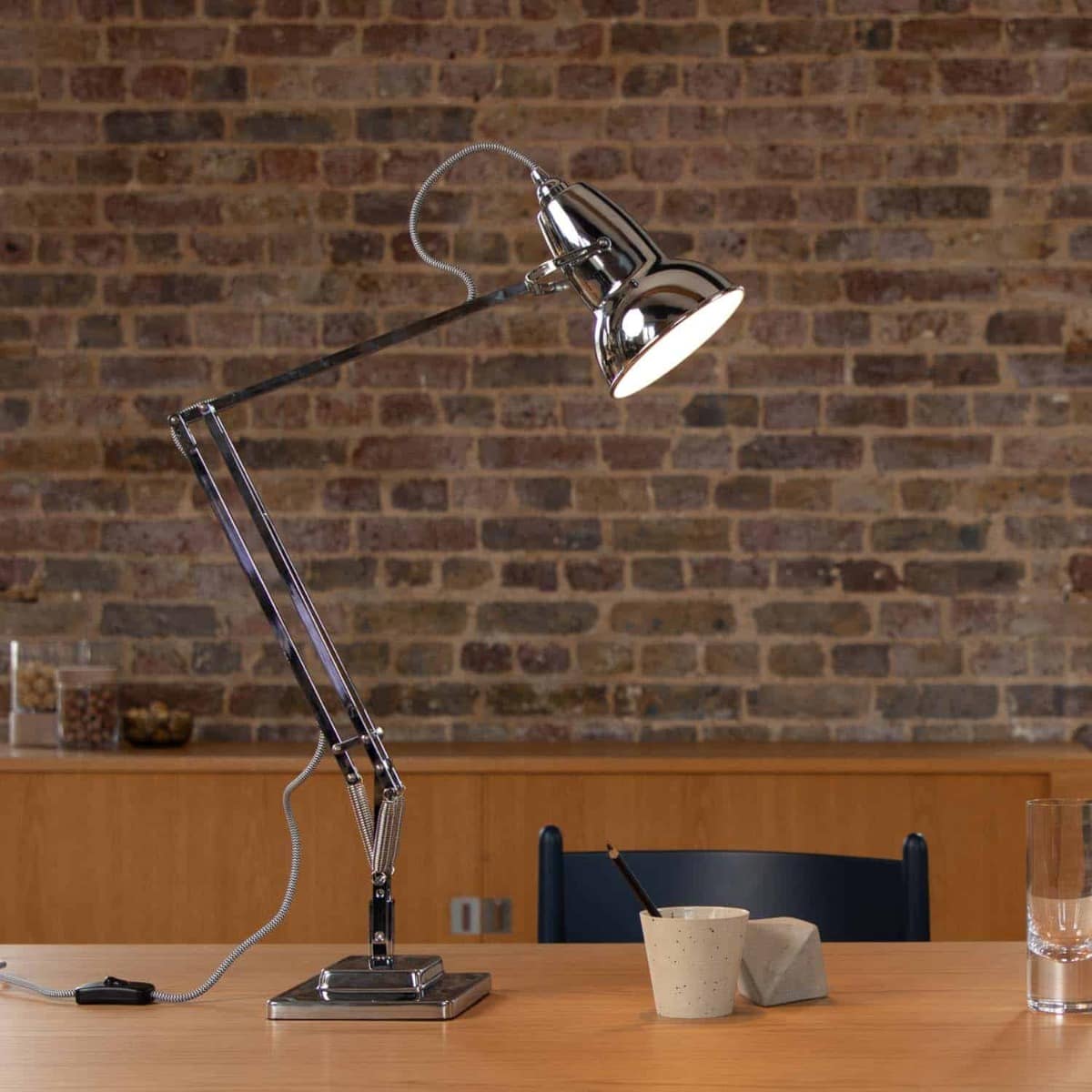 Anglepoise Original 1227 desk lamp in Bright Chrome on a wooden table against a brick wall