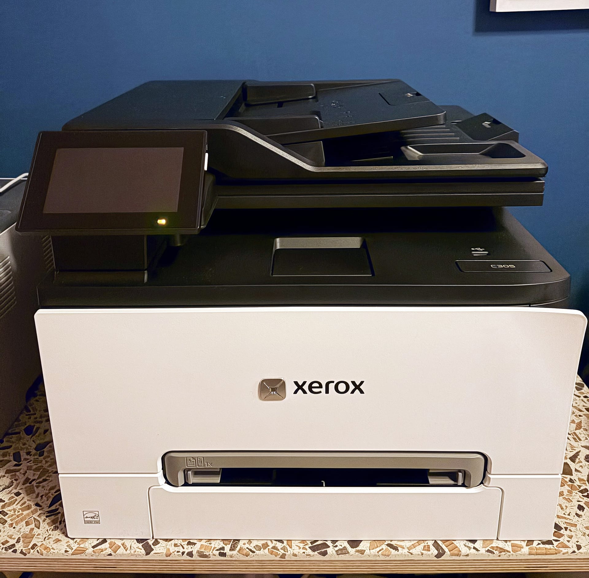 Xerox C305ae colour laser multifunction printer on a terrazzo desk against a dark blue wall