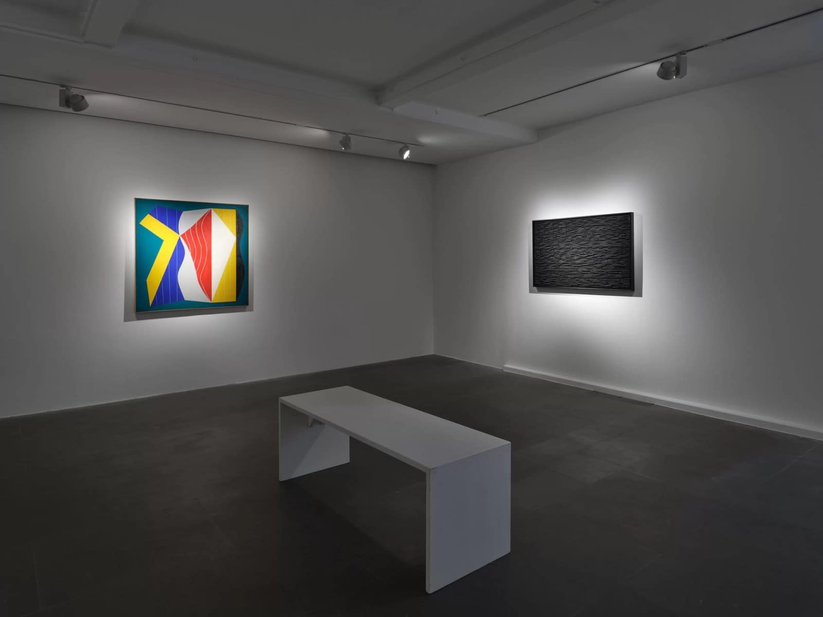A colourful geometric painting and a black relief by Ha Chong-Hyun in a dim gallery room at Lisson