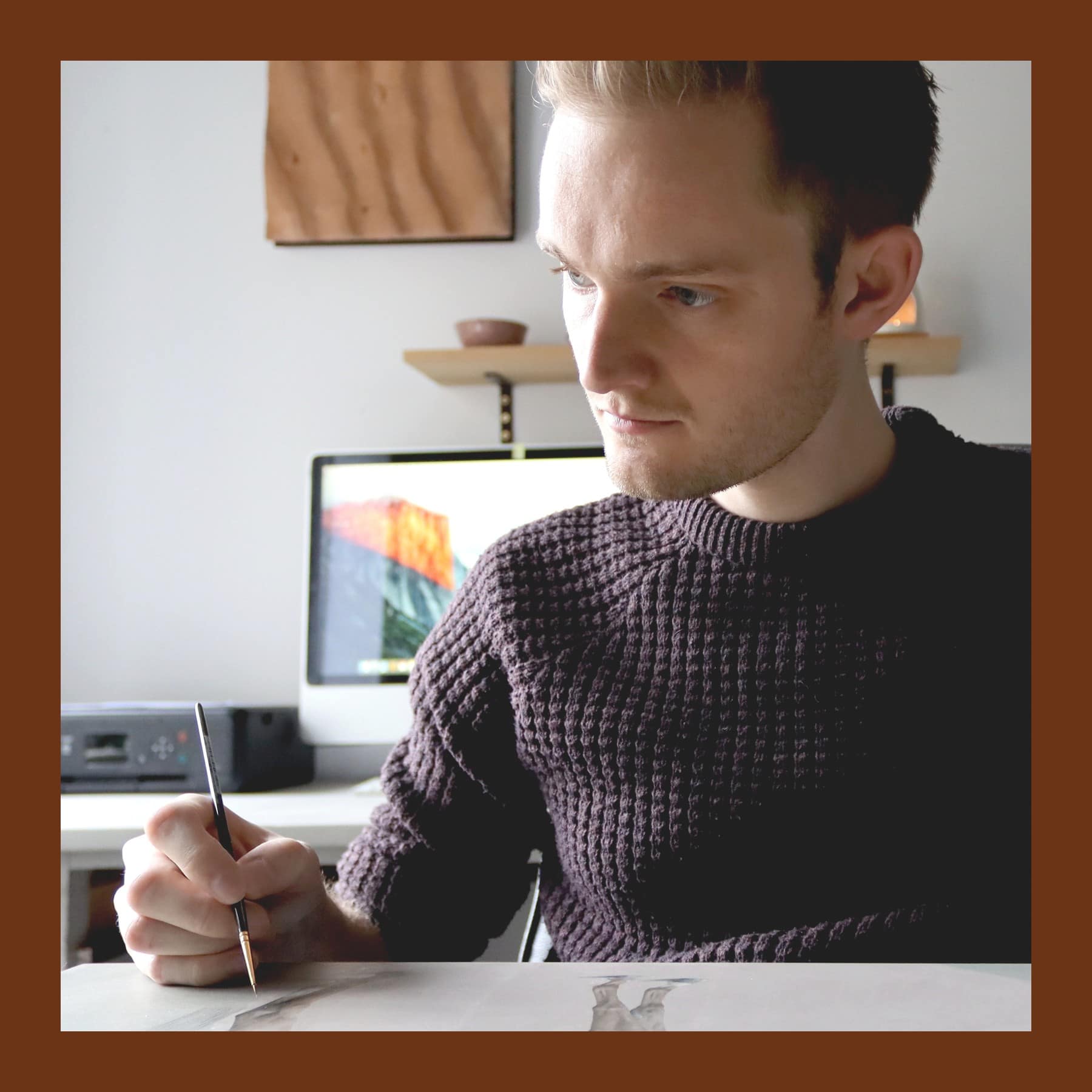 Joseph Black in a dark knitted jumper, painting a horse on paper with a fine brush at his desk