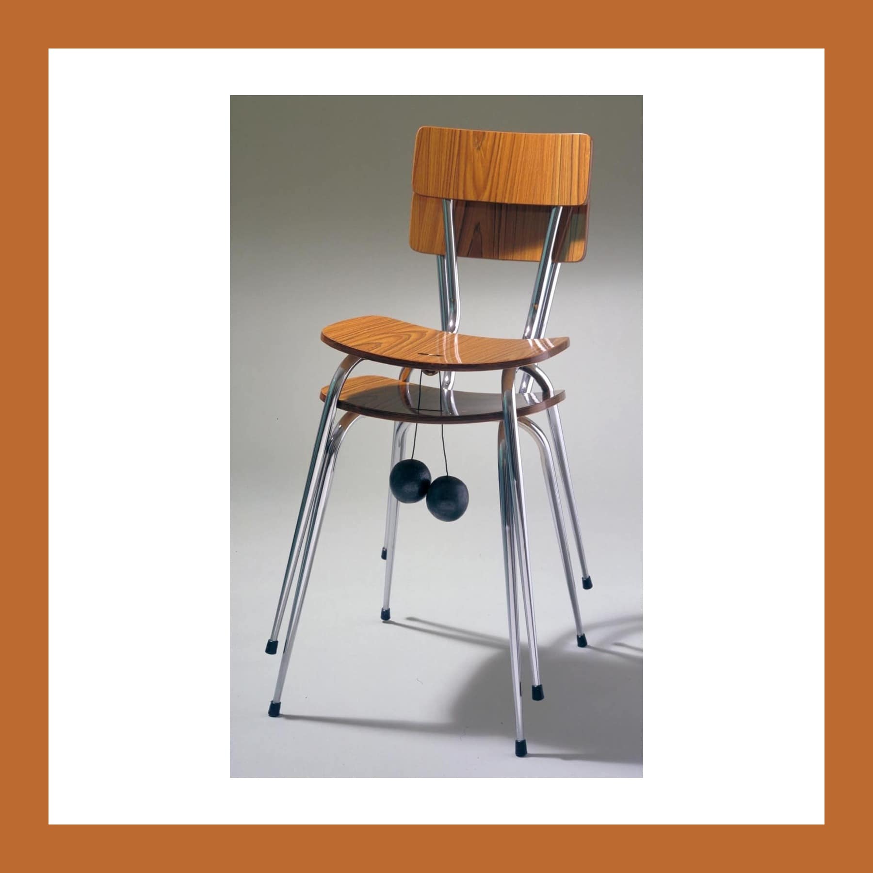 Sculpture of two stacked chrome-legged chairs with dark weights hanging from cables