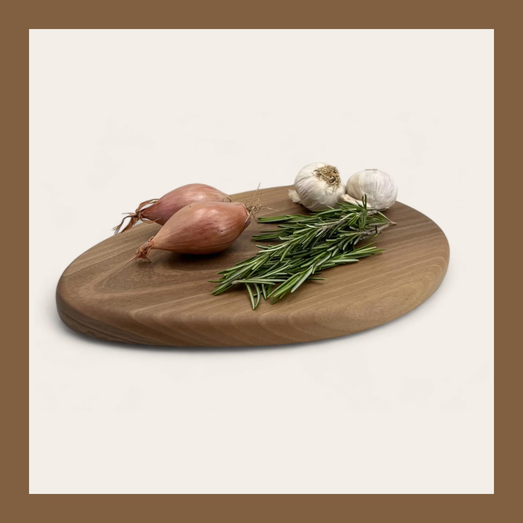 Fryth Pebble walnut chopping board with shallots, garlic and rosemary on a cream background