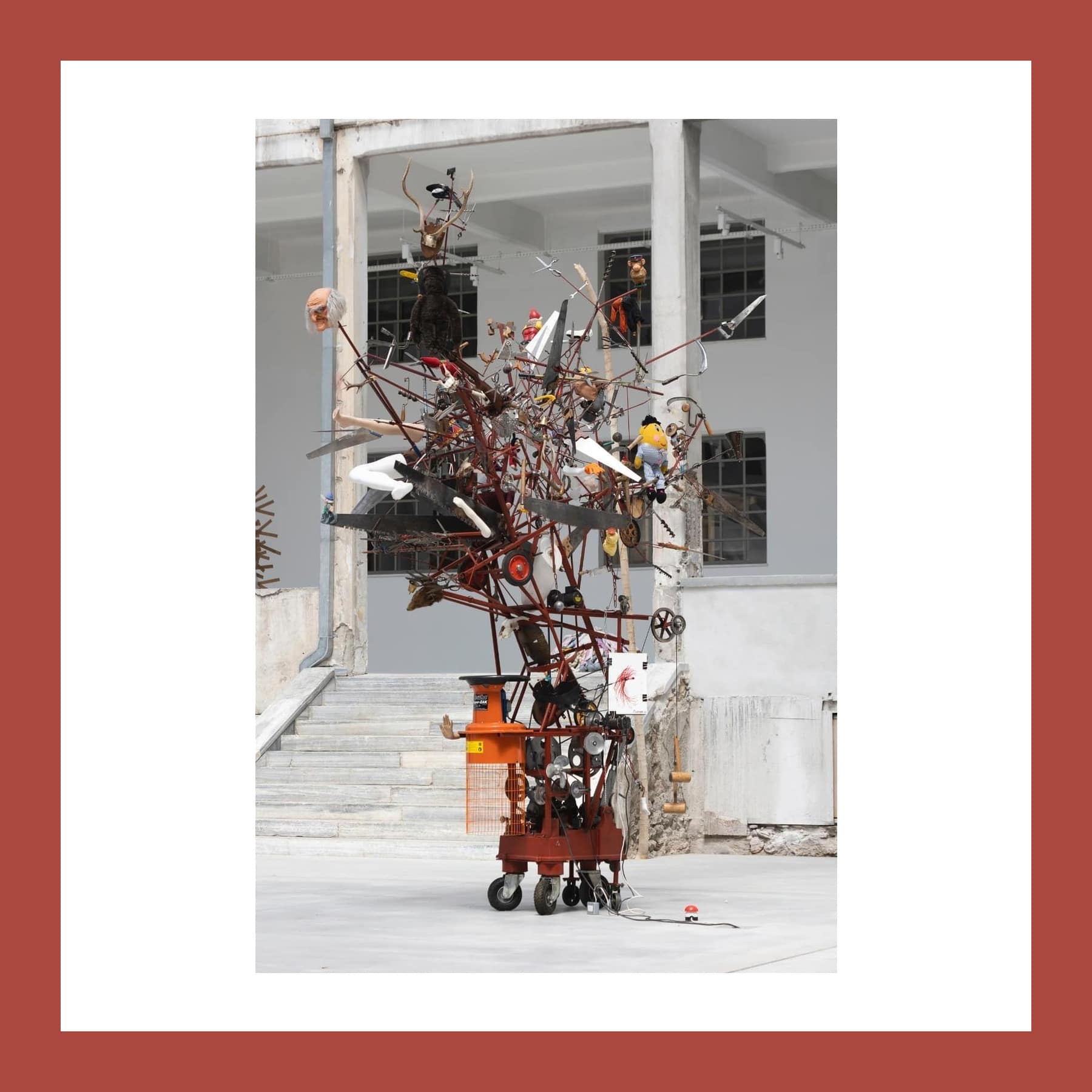 A tall, tangled sculpture of scrap metal, toys and machine parts on a wheeled trolley