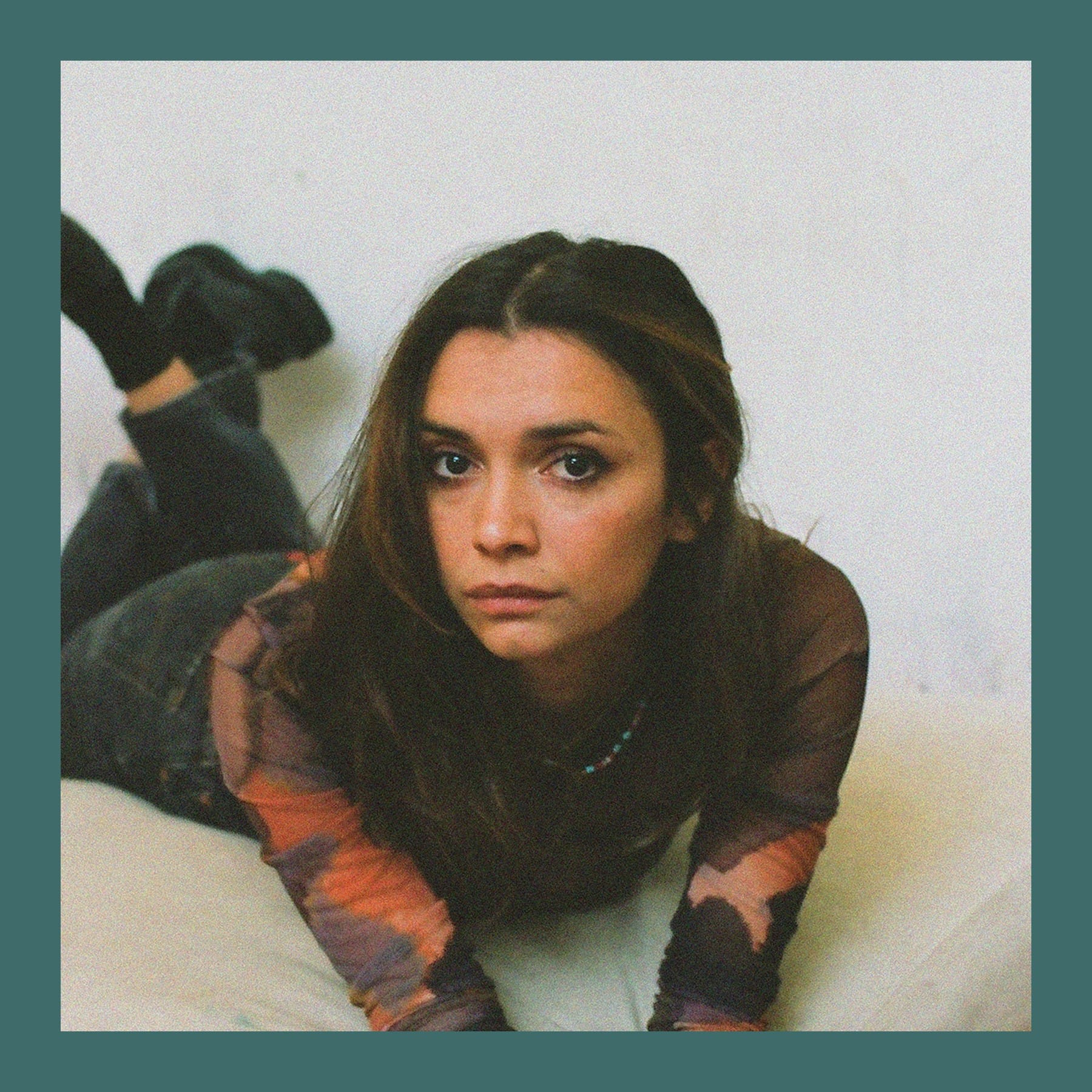Elizabeth Dimitroff, with long dark hair and a patterned top, lying on a floor cushion and looking at the camera
