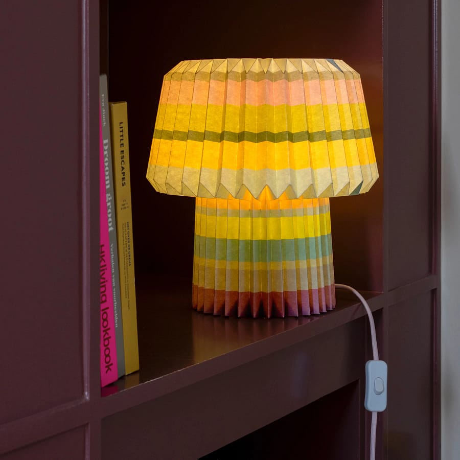Colourful REMEMBER® Anna pleated paper lamp glowing on a shelf