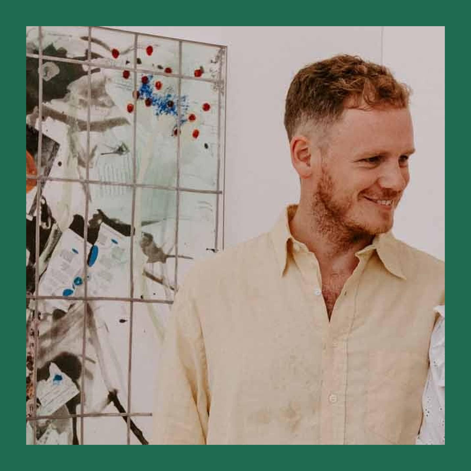 Charlie Billingham smiling in a pale linen shirt, standing beside an abstract painting in a white gallery
