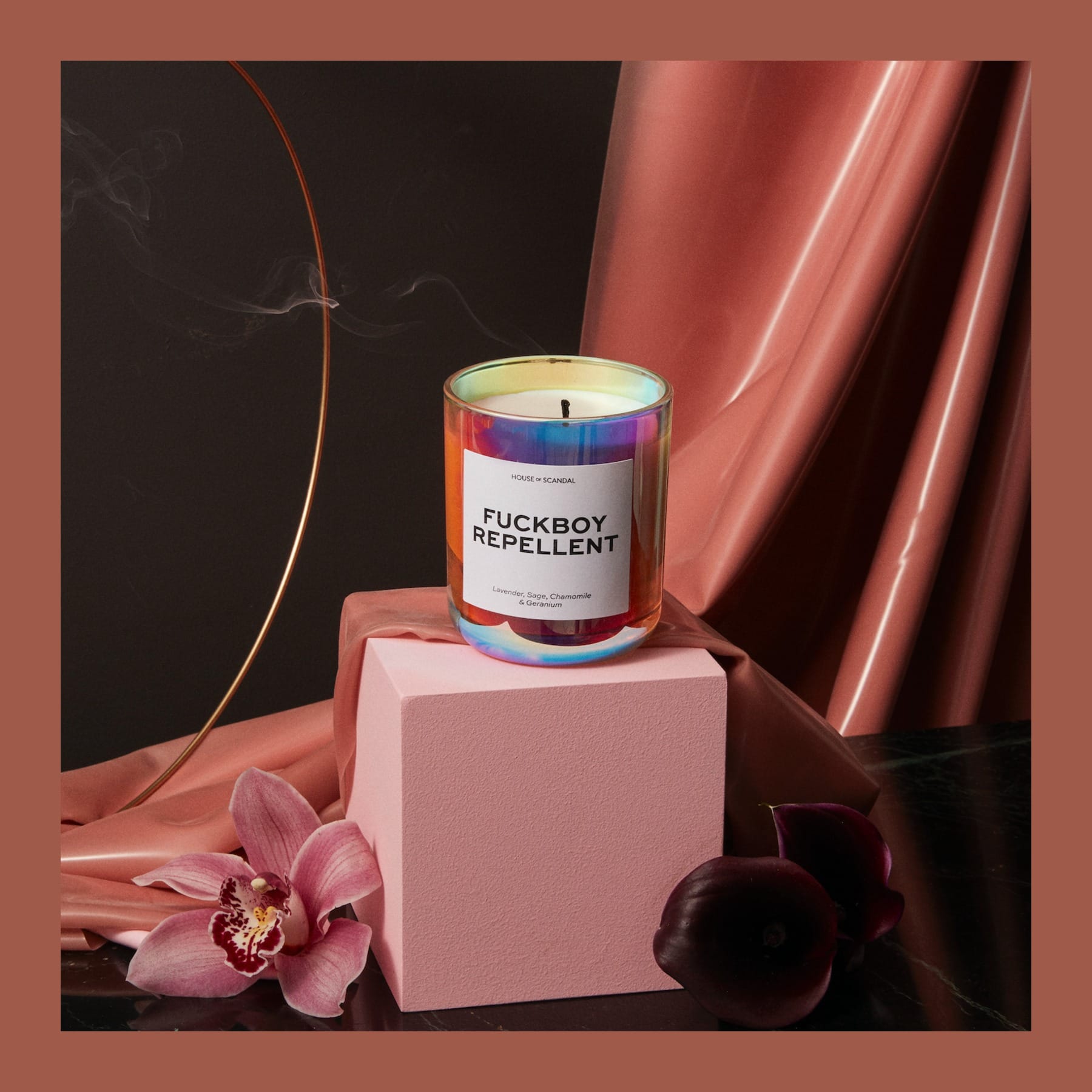 House of Scandal Fuckboy Repellent candle in an iridescent glass jar on a pink plinth with orchids